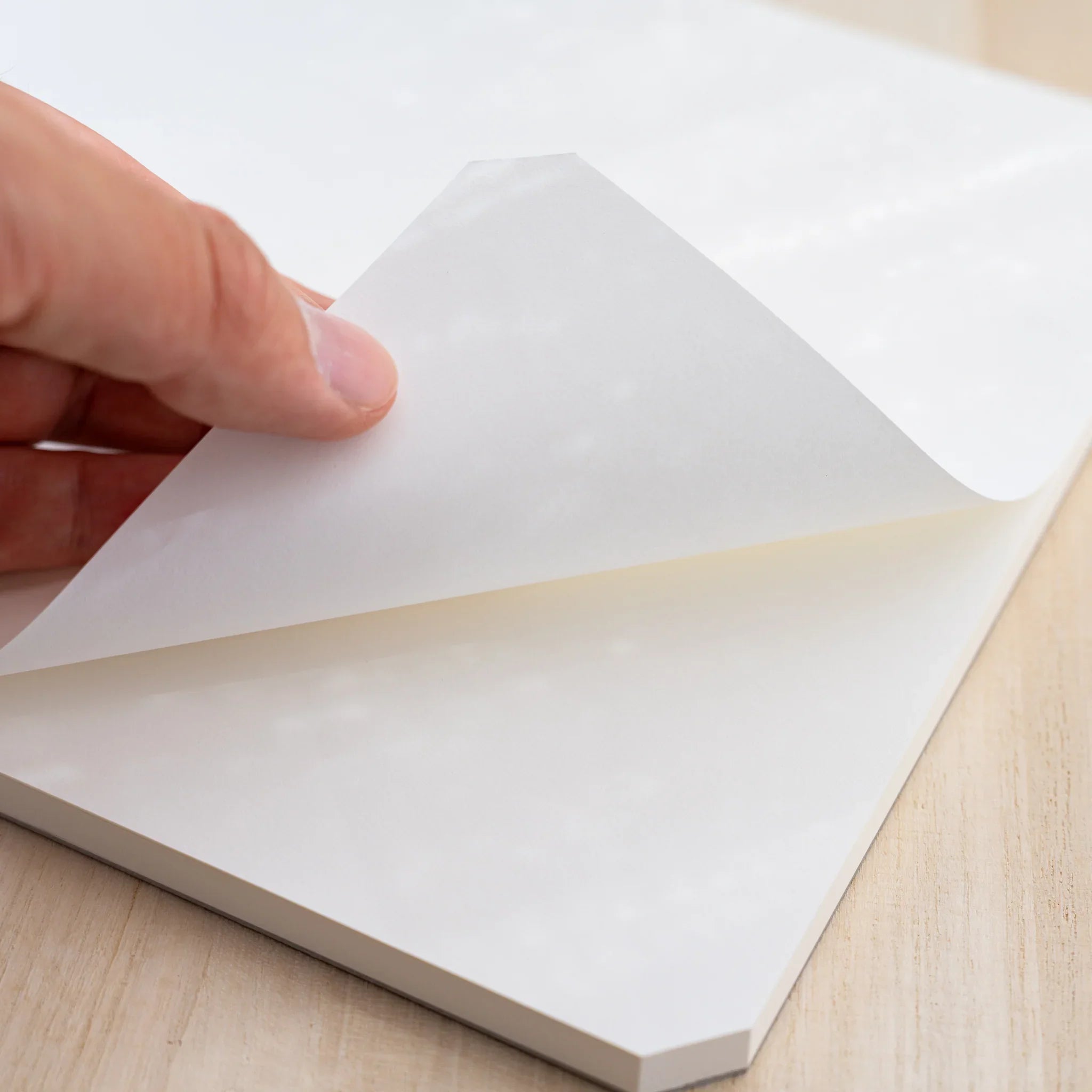 A hand lifting the blank white top sheet of a Midori MD Paper Pad Cotton A4, cut corner visible