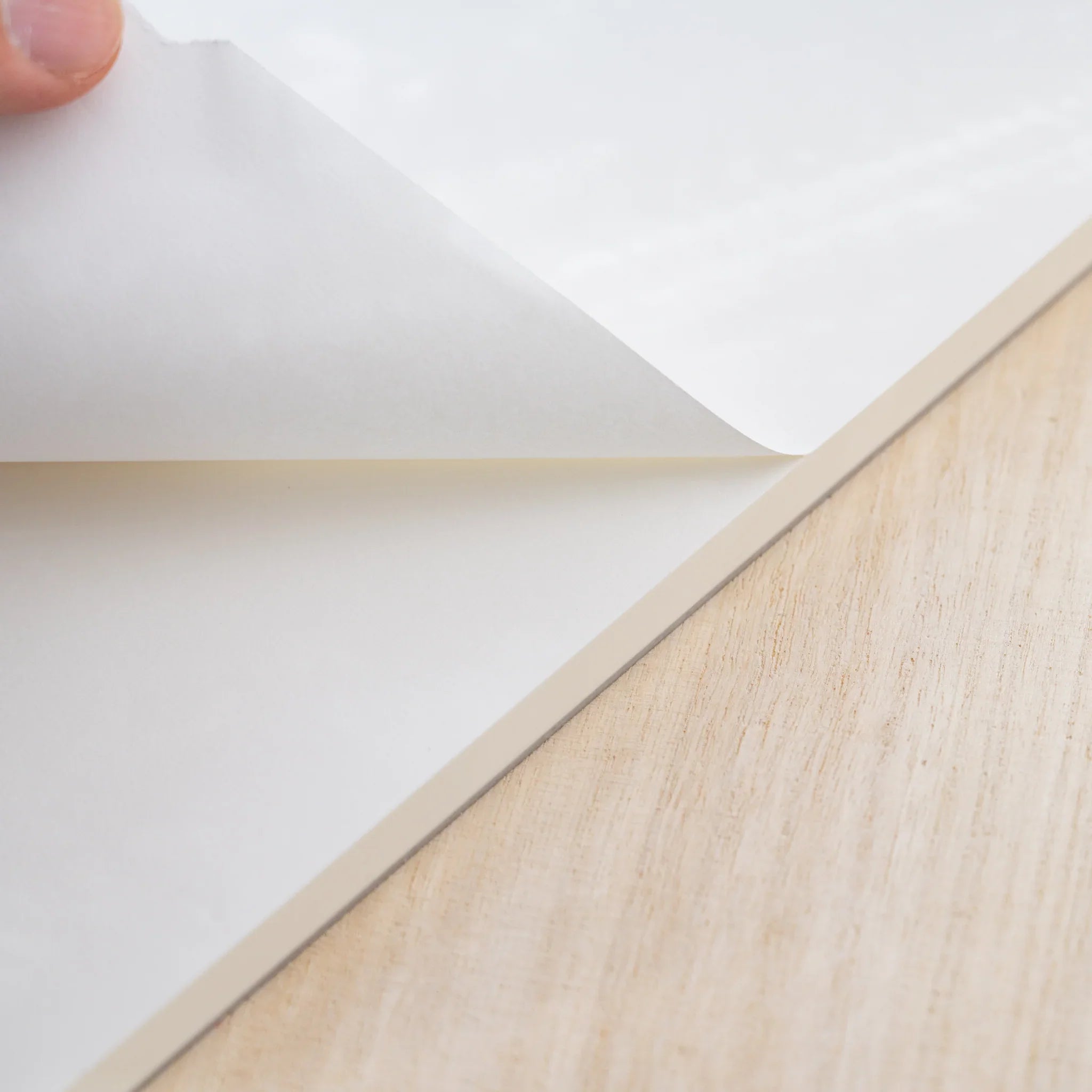A hand peeling a blank white sheet from the glued top edge of a Midori MD Paper Pad Cotton A4