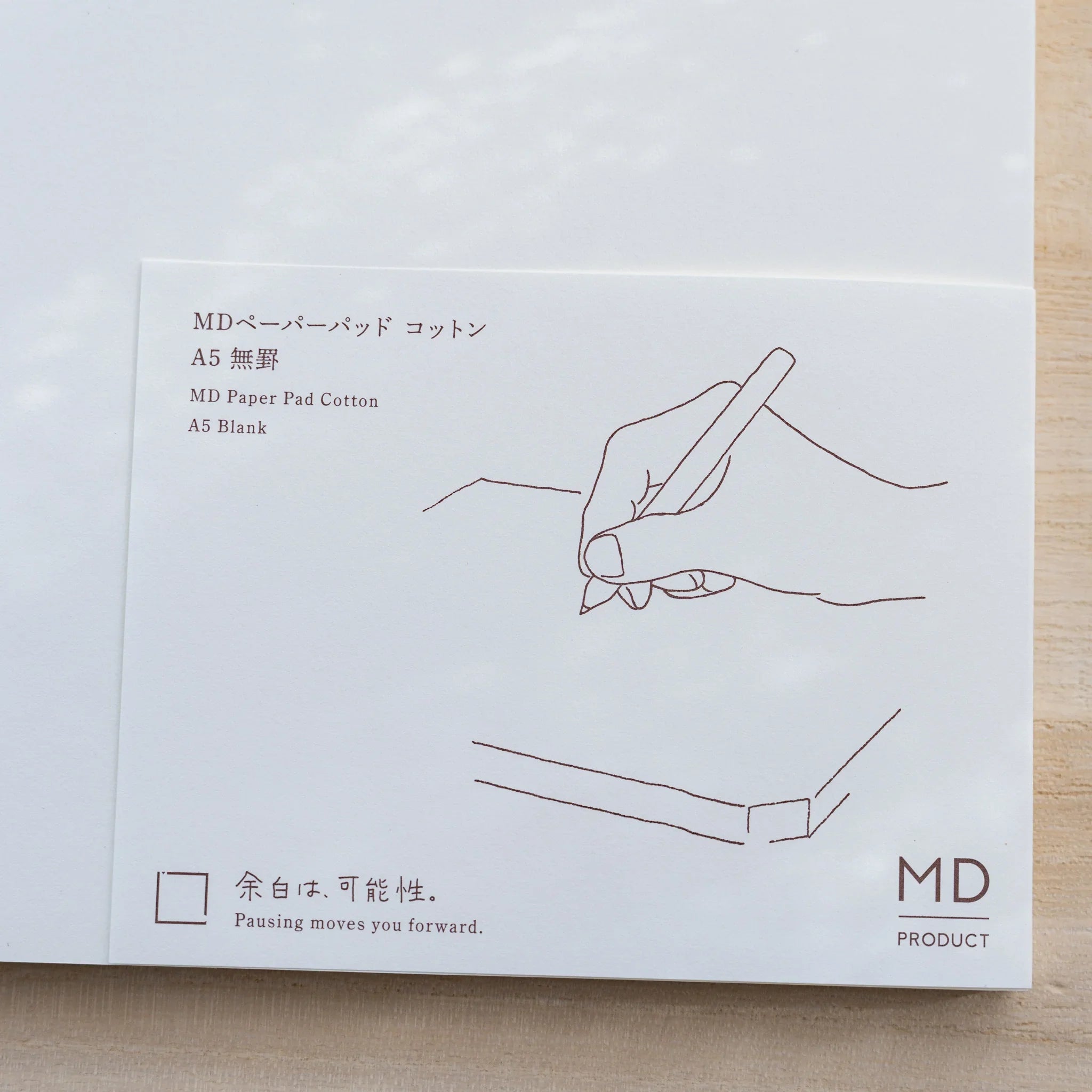 Close-up of Midori MD Paper Pad Cotton A5 belly band in brown, hand-writing line drawing and MD Product logo