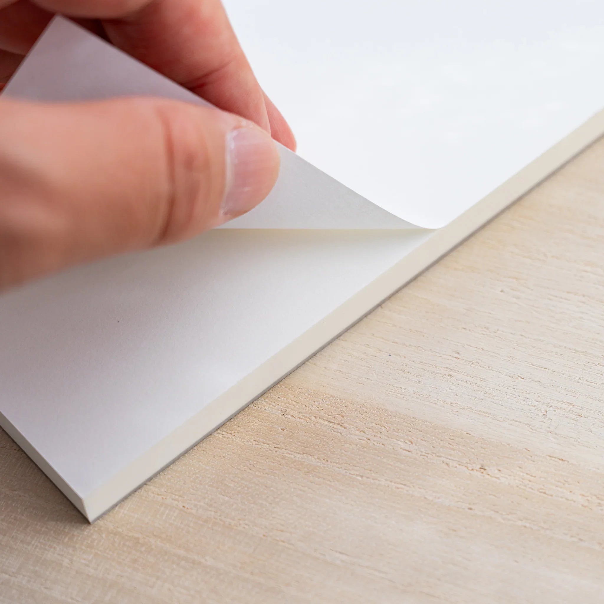 A hand peeling a blank white sheet from the glued top edge of a Midori MD Paper Pad Cotton A5