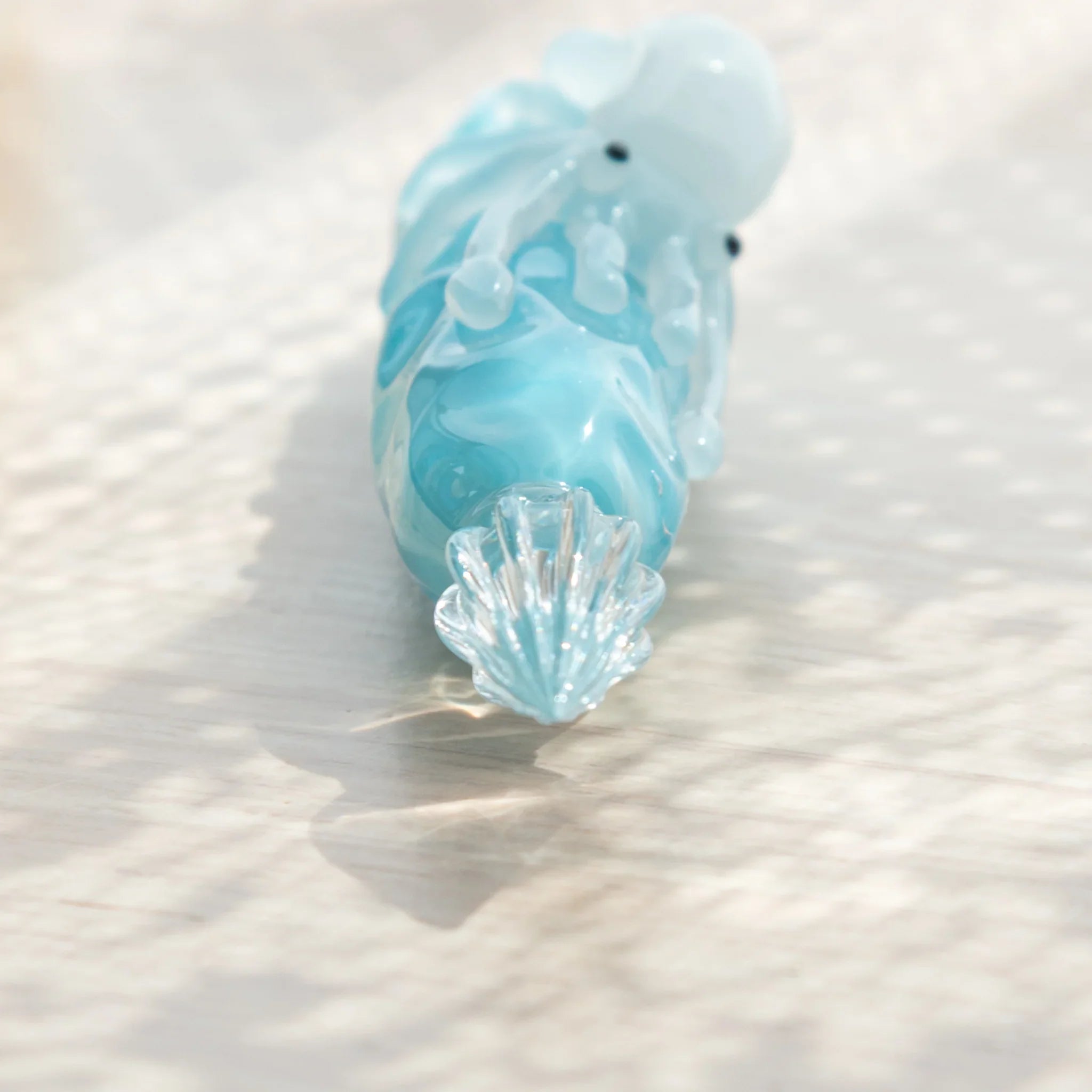 Macro close-up of ribbed glass nib on light blue glass dip pen, white squid figure and blue barrel visible above