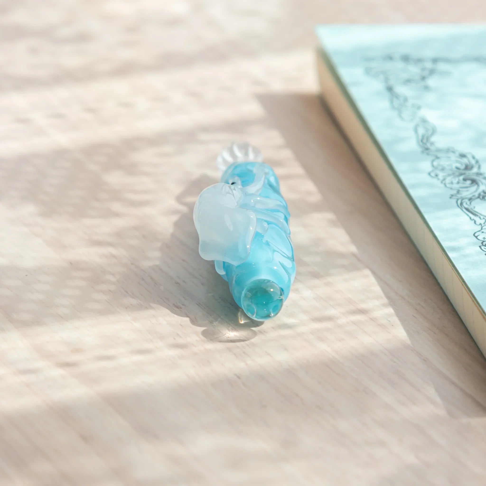 Light blue glass dip pen viewed from end cap side showing clear glass ball end and blue barrel with white squid figure
