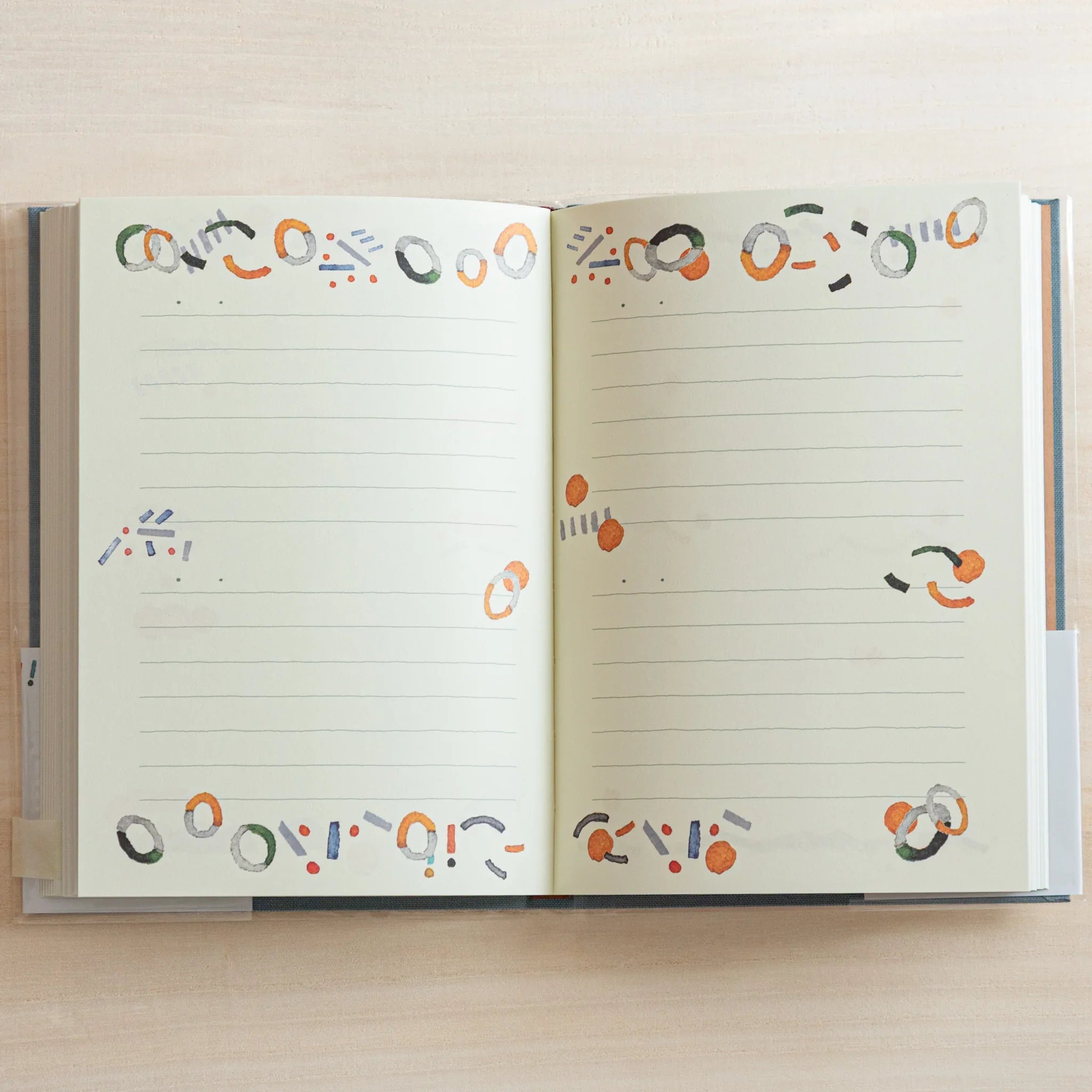 Open Midori Japanese journal showing lined pages decorated with colorful ring and dot motifs around edges.