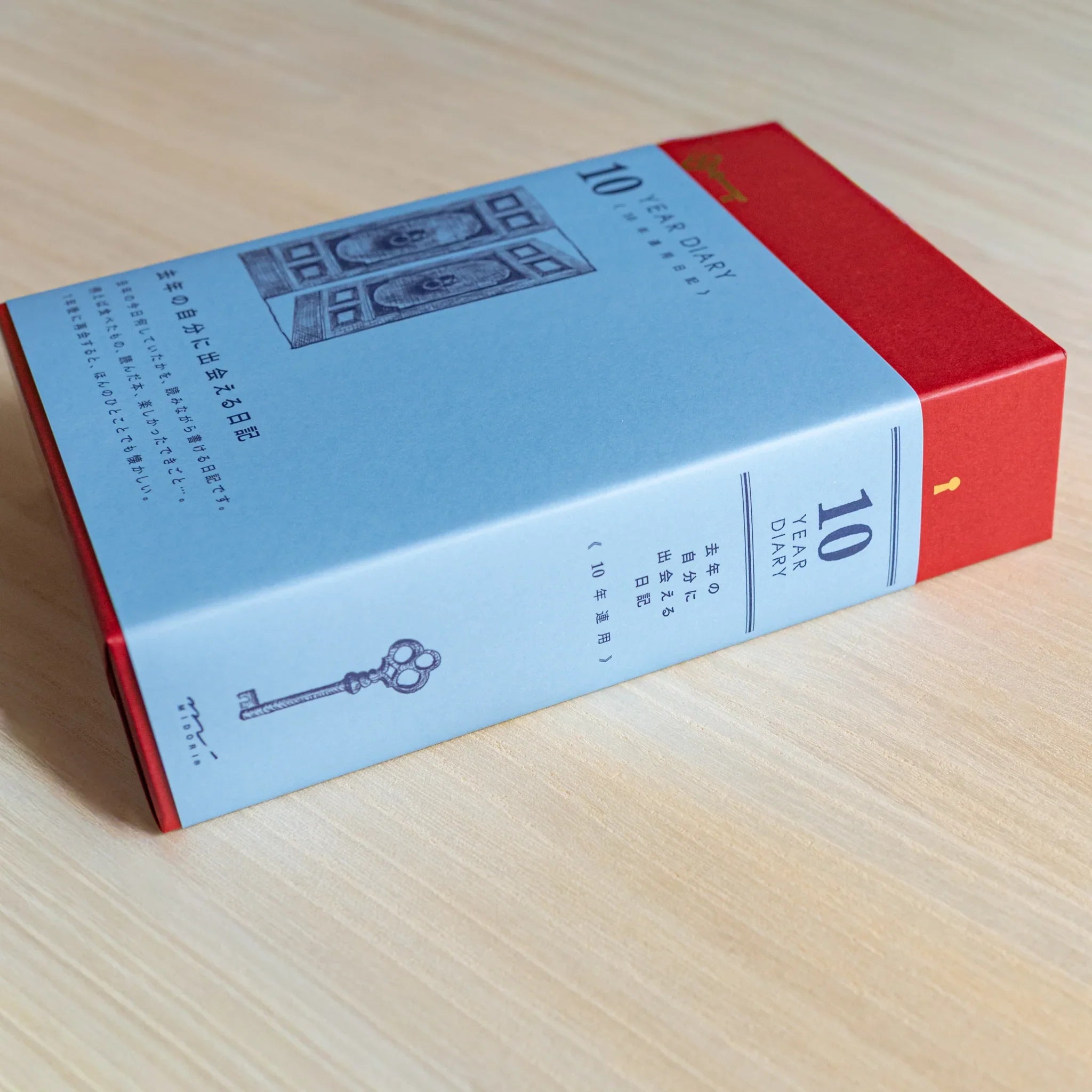 Midori Japanese journal 10-year diary gate design red and blue slipcase lying on its side on wooden surface.