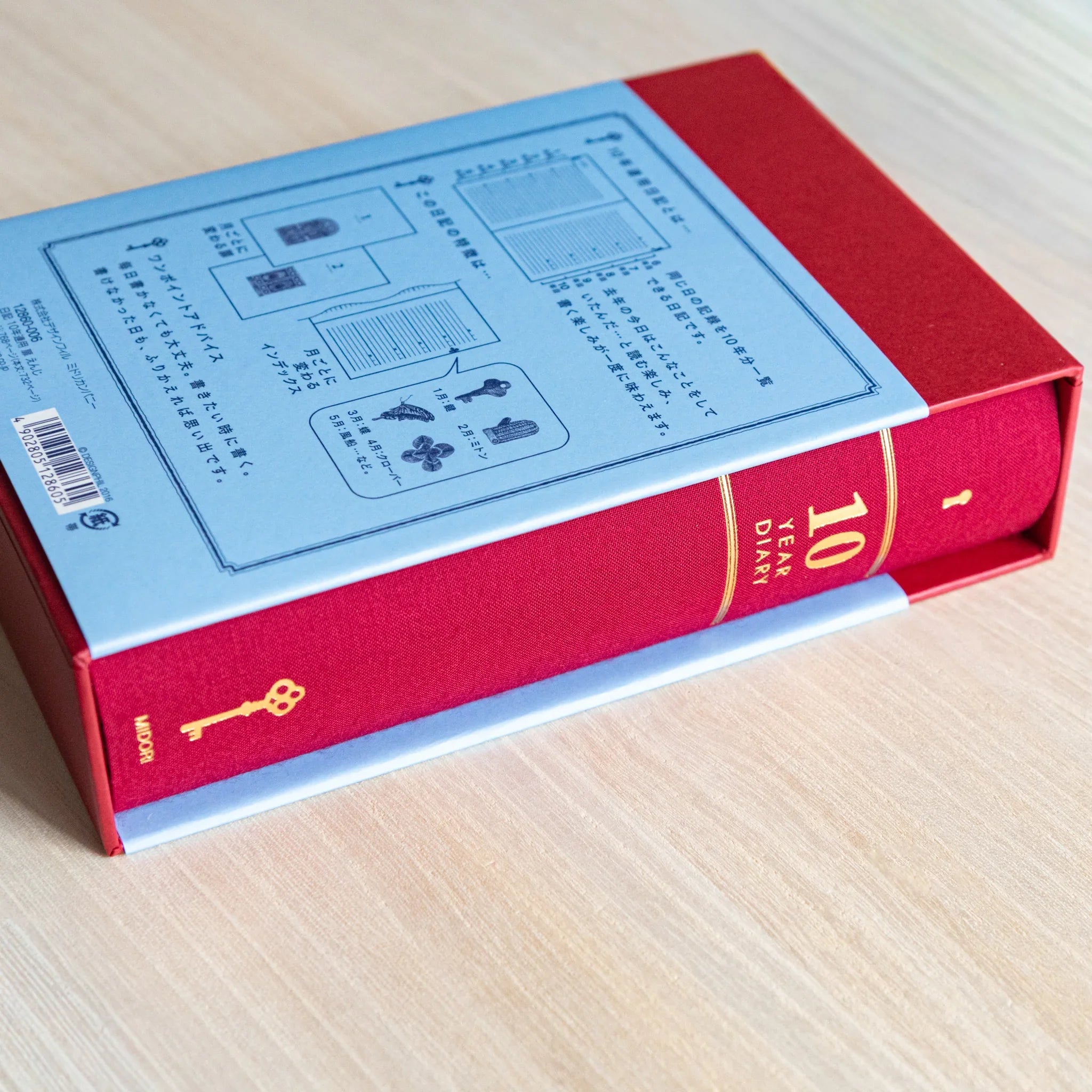 Midori Japanese journal 10-year diary gate design red book in blue slipcase sideways on wooden surface.