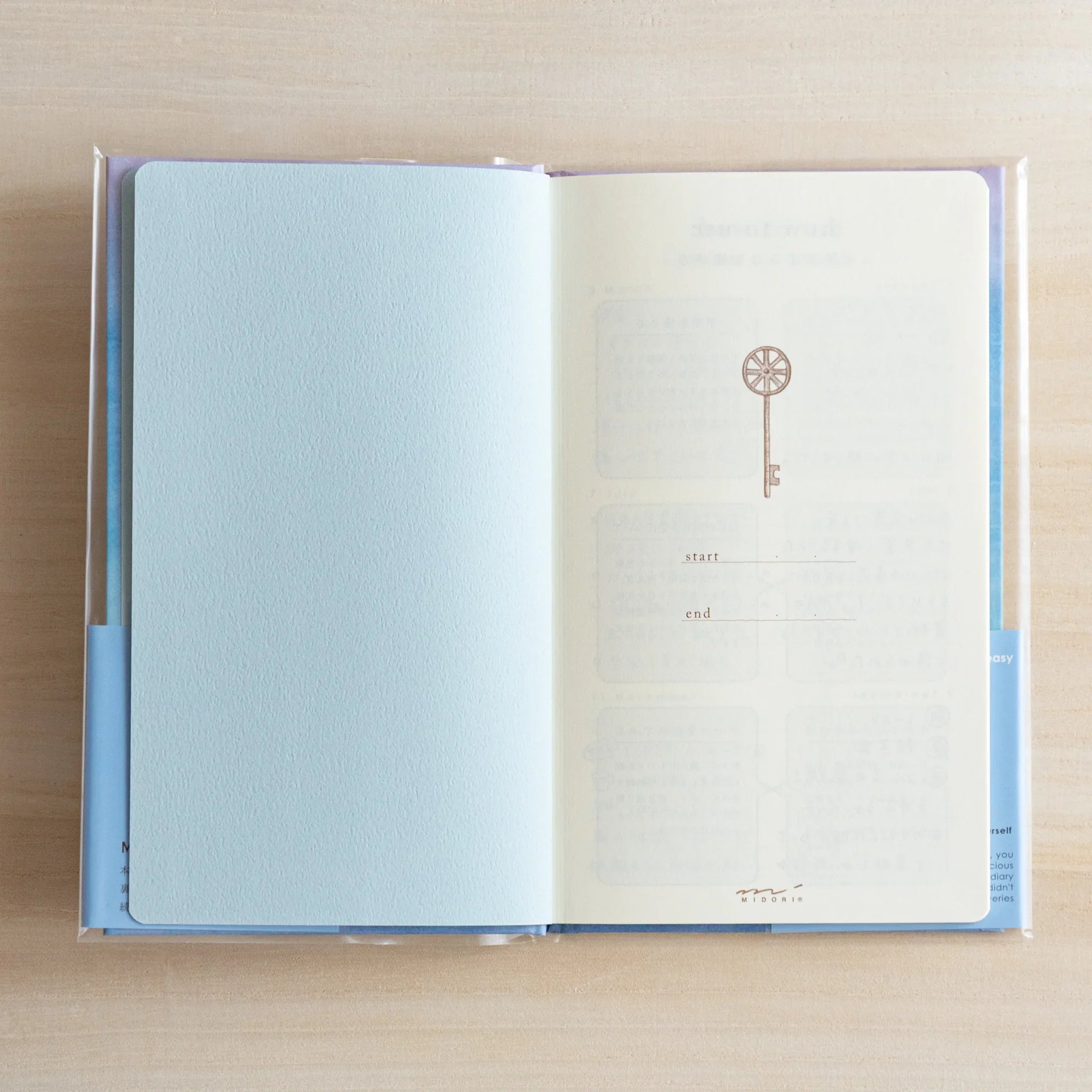 Open Midori Japanese journal pages with blank sheet opposite a faint key motif and date boxes.