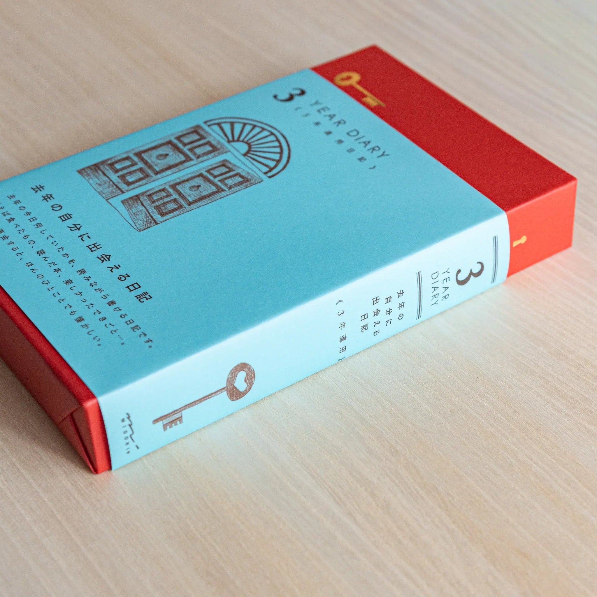 Side view of Midori Japanese journal 10-year diary gate design showing light blue spine with key illustration and red top.