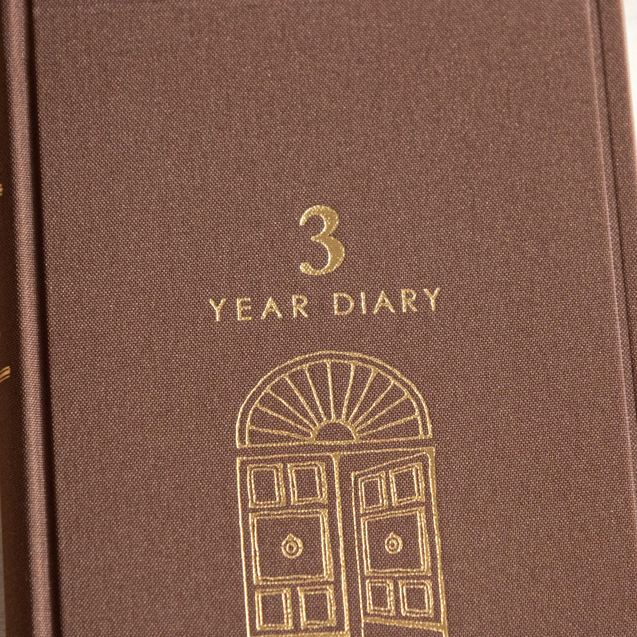 Close-up of the Midori Japanese journal, featuring a brown cloth cover with elegant gold-embossed lettering and door motif.
