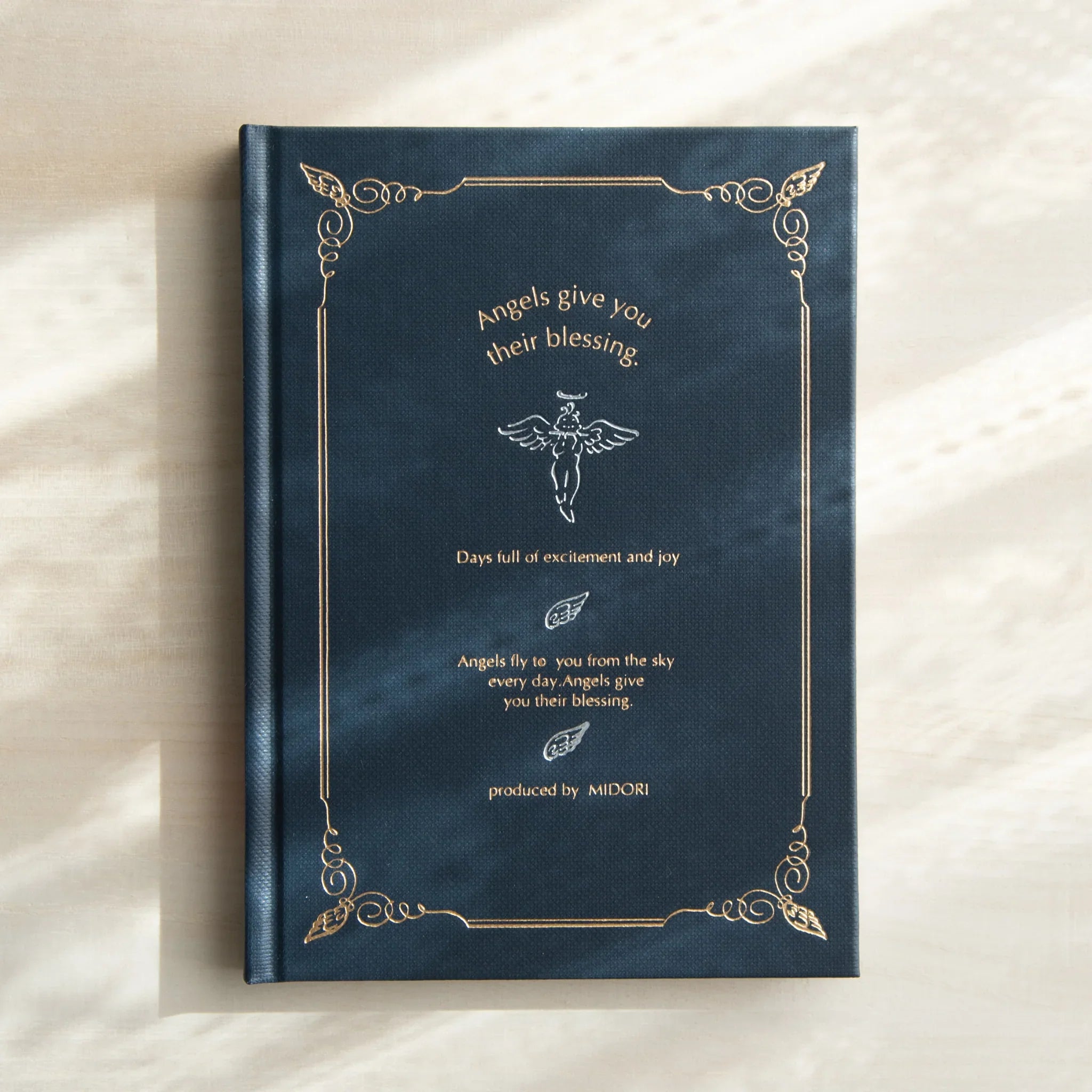 Dark blue hardcover notebook with embossed gold angel figure and ornamental decorative border motif design throughout cover