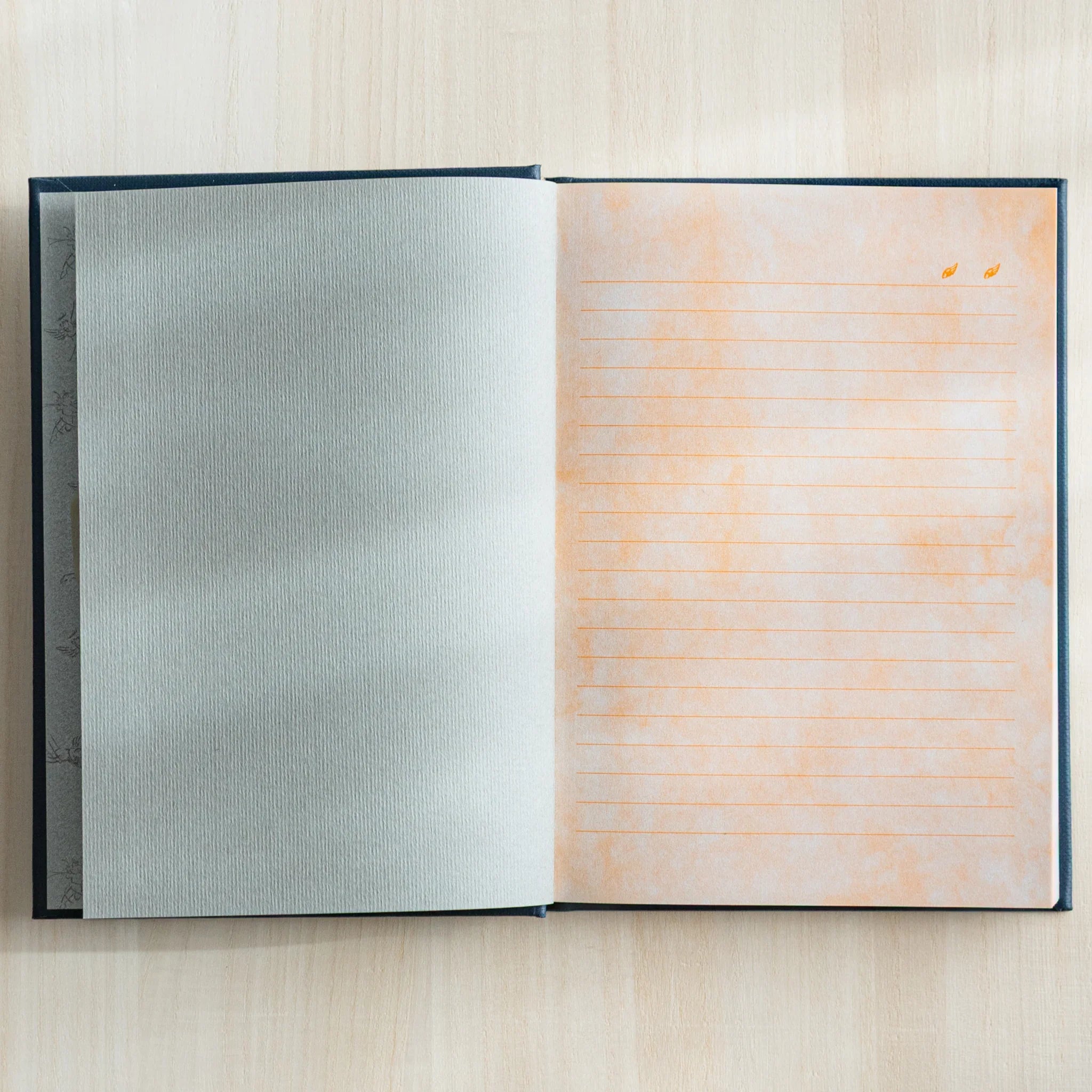 Flat lay of open notebook showing cream and peach colored lined pages with decorative angel designs throughout