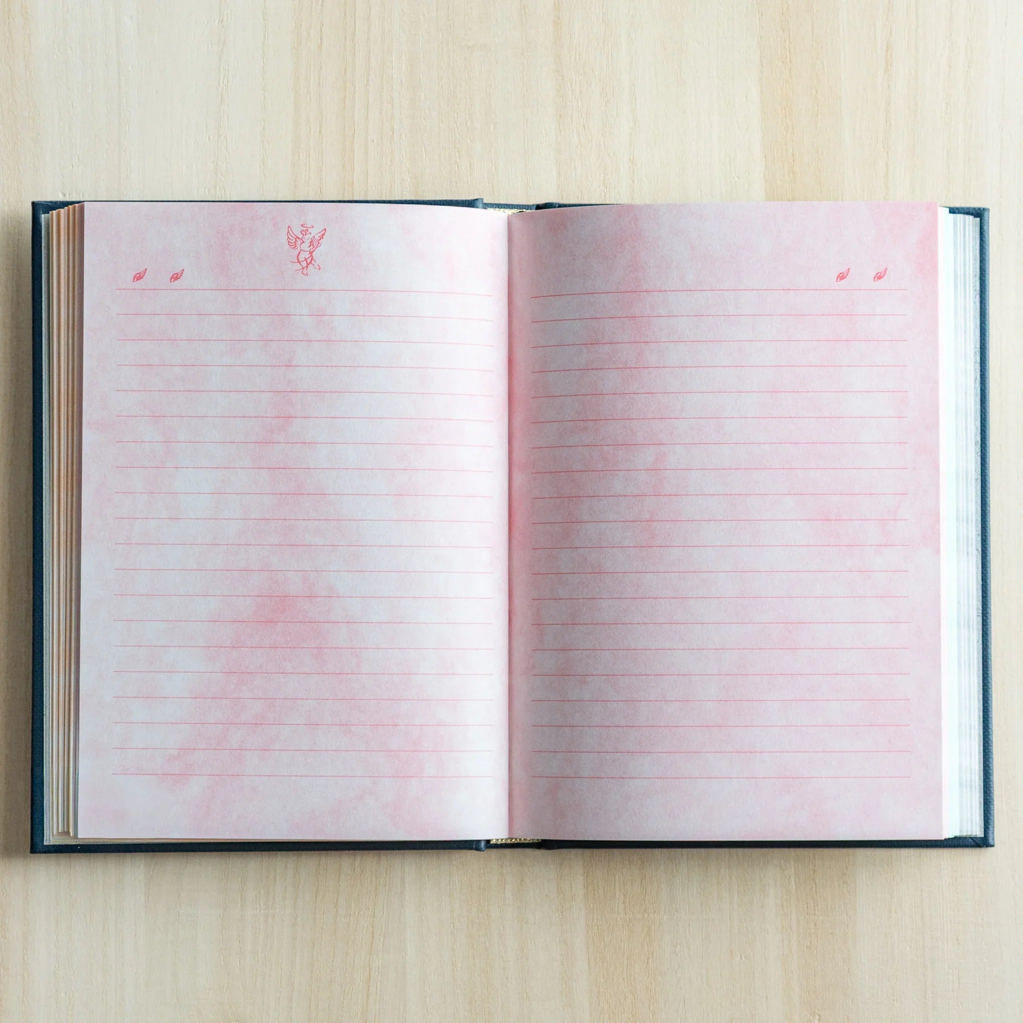 Open journal displaying pink-tinted interior pages with repeating angel watermark design pattern visible clearly