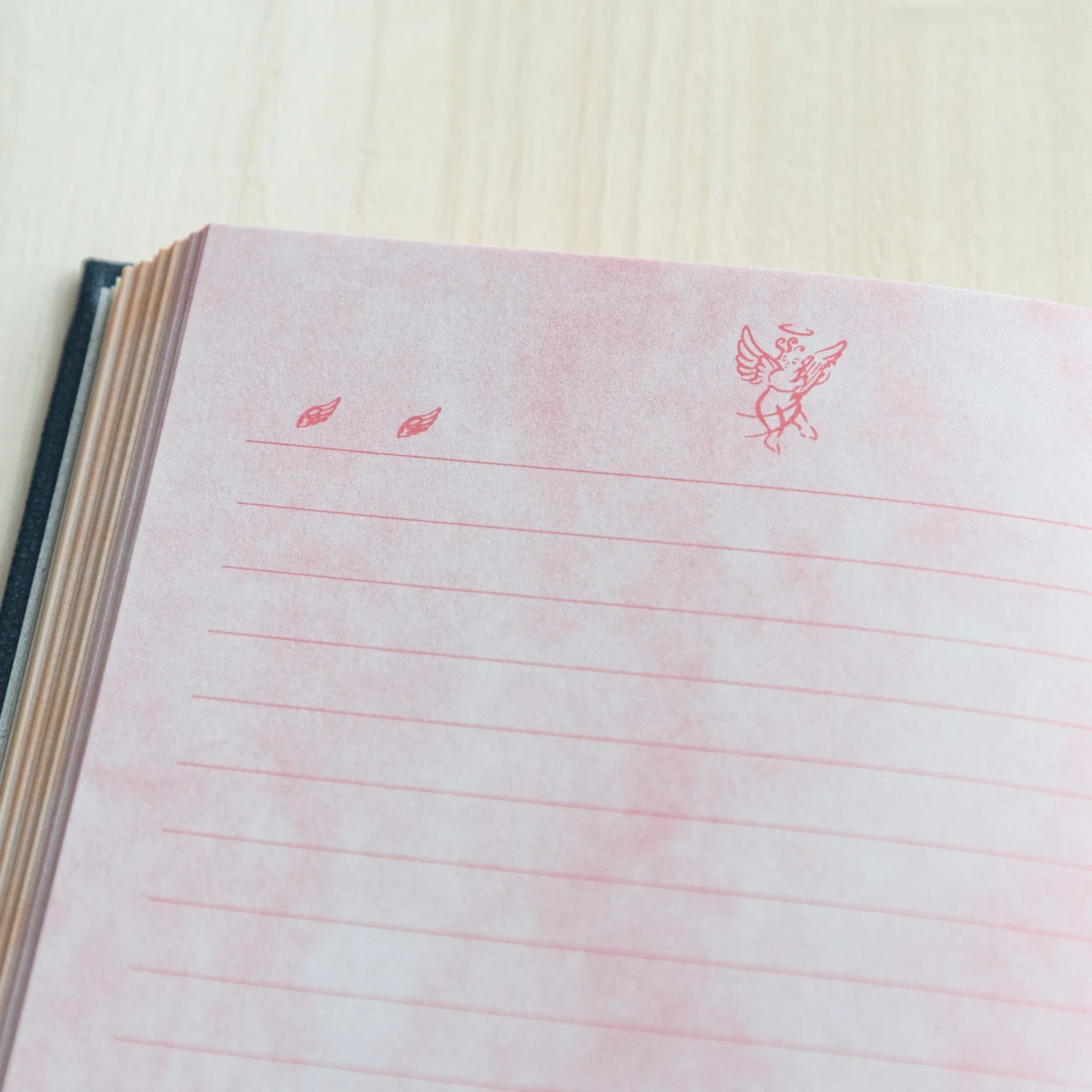 Close-up view of pink ruled notebook page with angel figure decoration positioned in upper corner area clearly