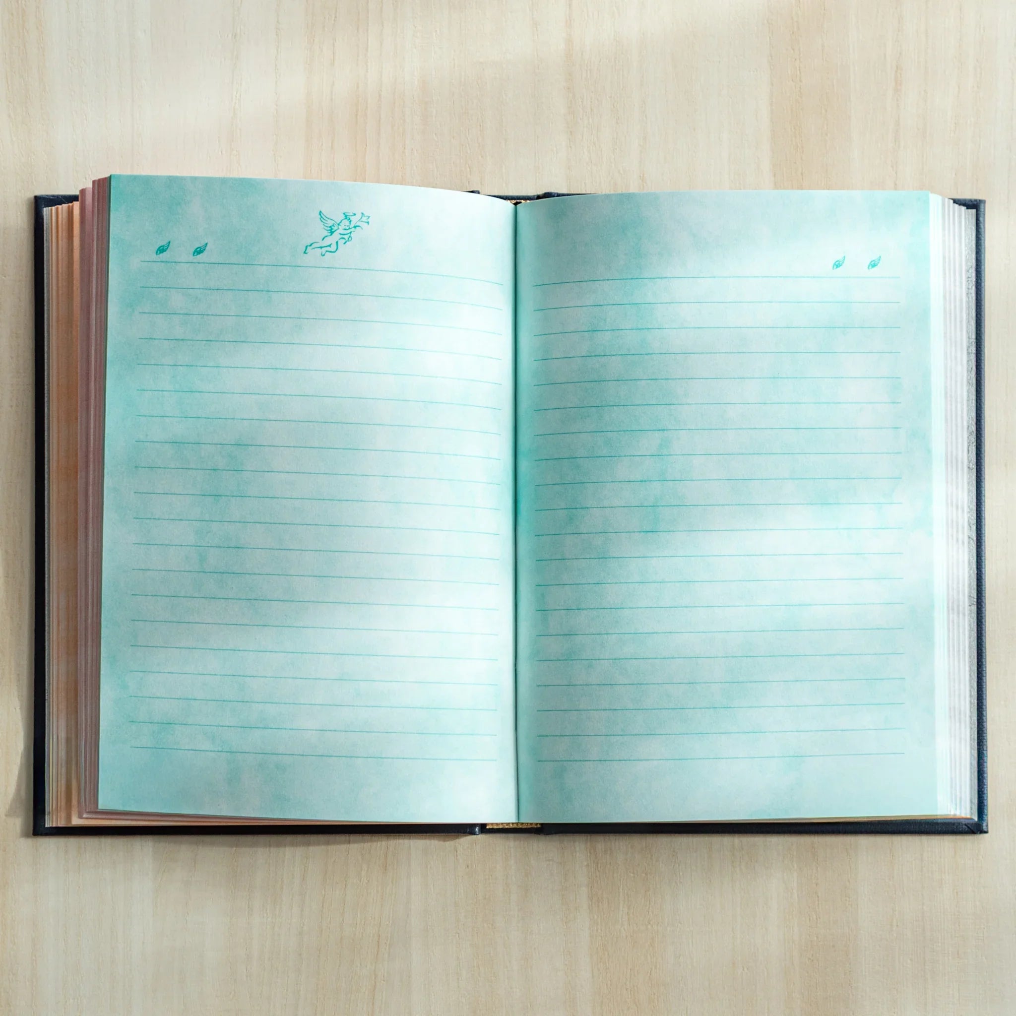 Journal open to turquoise-blue interior pages with angel motif pattern and horizontal writing lines visible