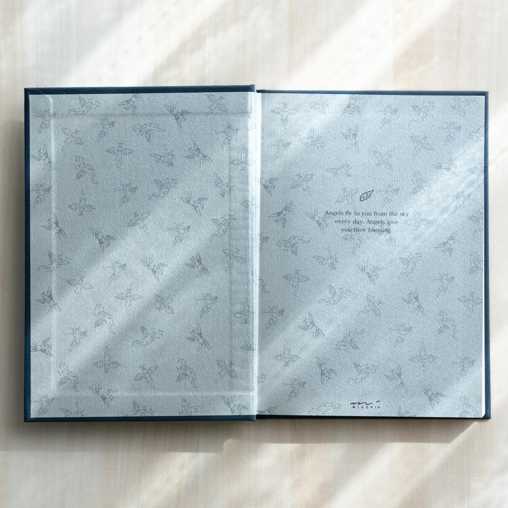 Inside cover of Midori Angel Motif Journal open flat, featuring pale gray endpaper printed with delicate angel motif pattern