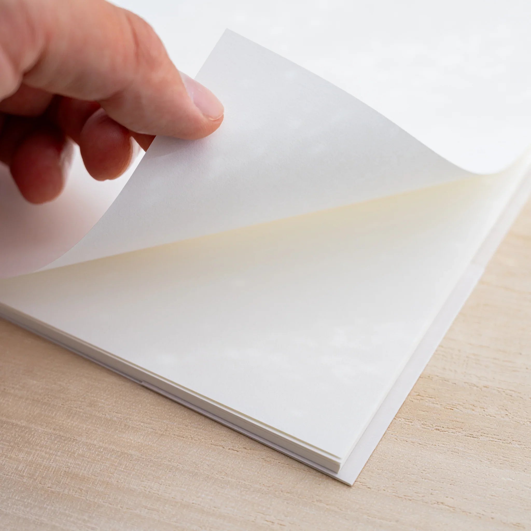 A hand lifting a blank cream cotton page of an open Midori MD Cotton Notebook A5