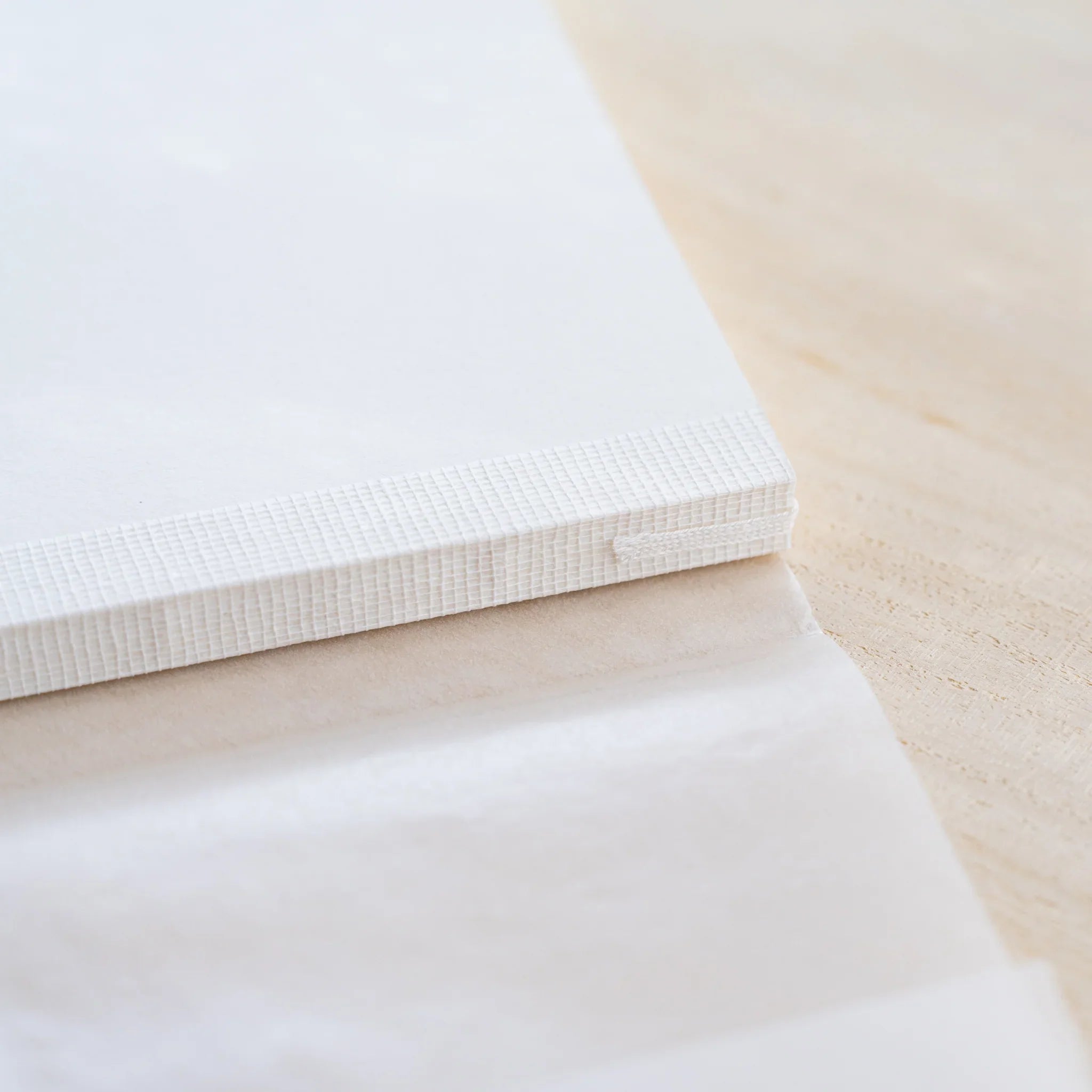 Close-up of Midori MD Cotton Notebook A5 textured white cover edge and exposed thread binding at the spine