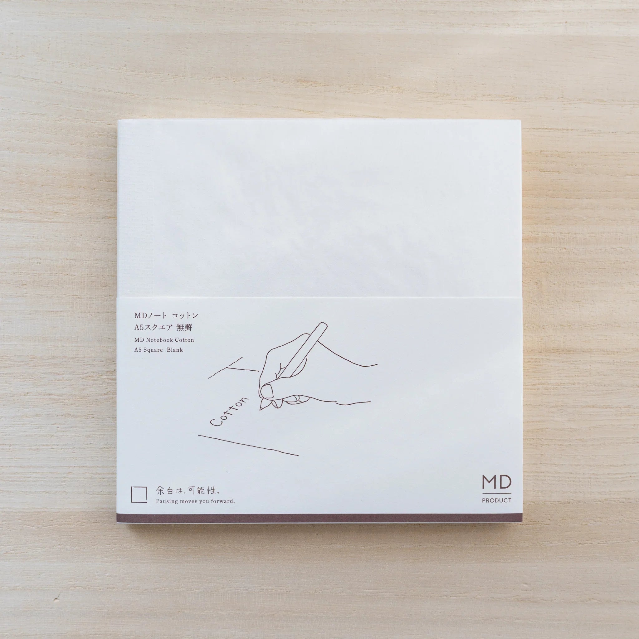 MD Cotton Notebook A5 Square in cream cover with paper belly band showing a hand-with-pen line drawing