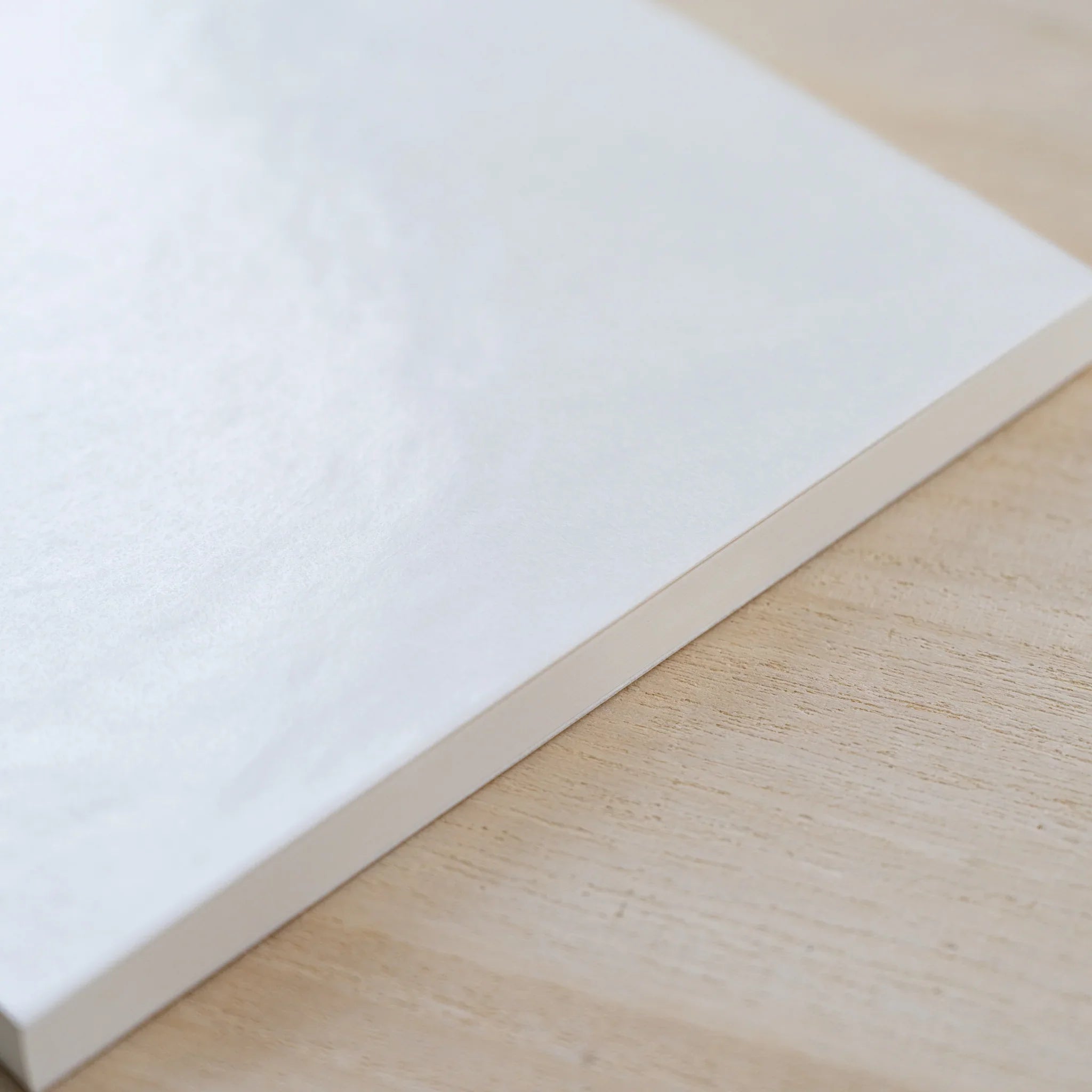 Angled view of the closed square cream MD Cotton Notebook A5 Square on a wood surface