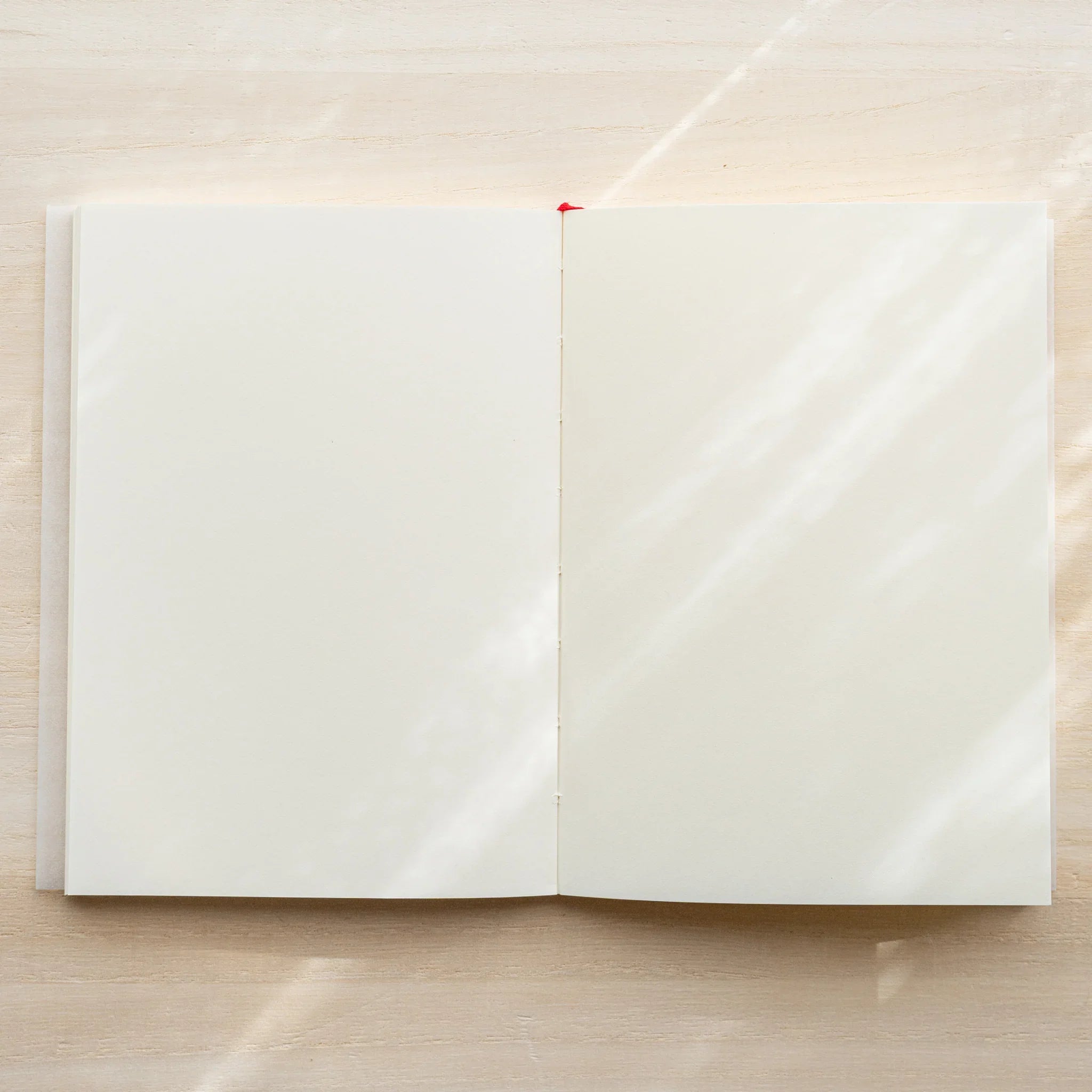 Midori MD Notebook A6 Blank opened flat showing blank ivory page spread, red bookmark ribbon visible at center spine