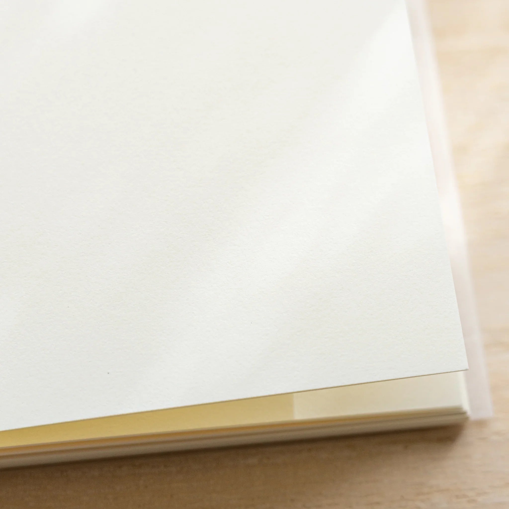 Midori MD Notebook A6 corner close-up, blank ivory page with translucent glassine cover, belly band visible at bottom edge
