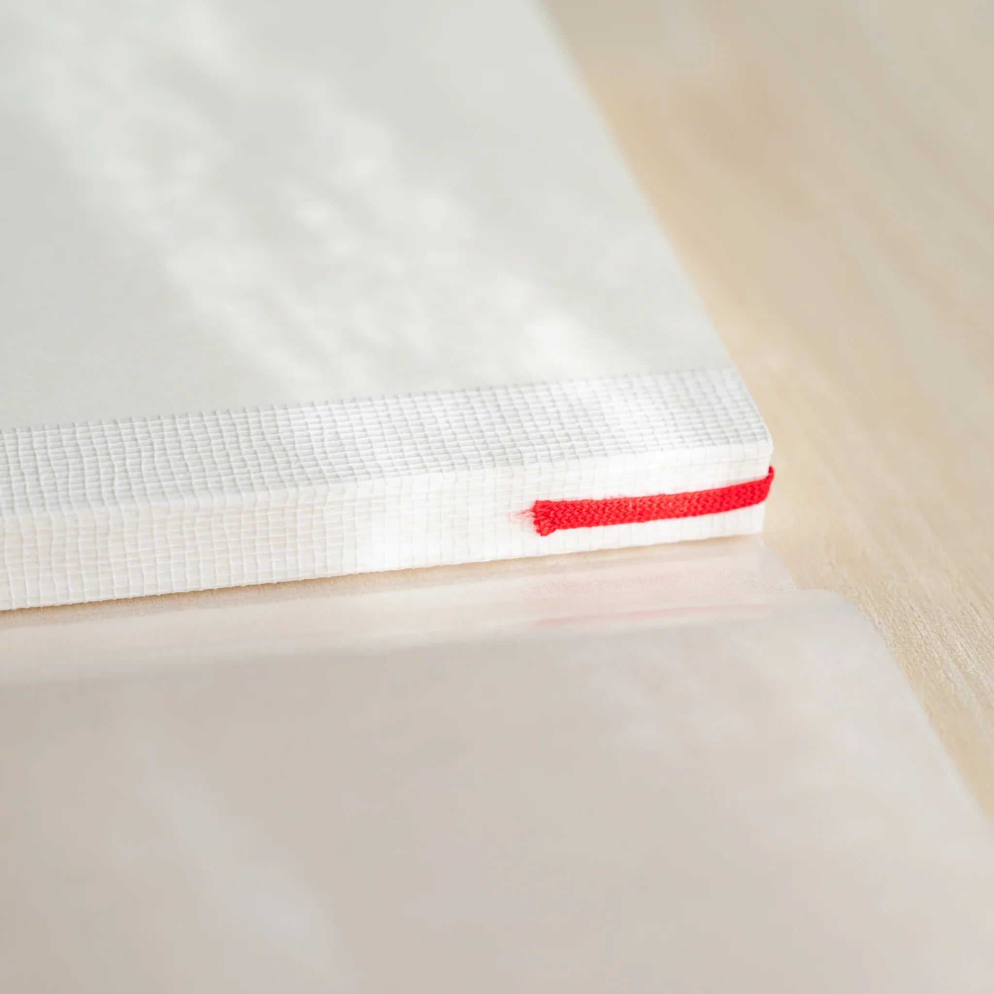 Midori MD Notebook A6 spine close-up showing white thread-stitched binding with red bookmark ribbon at bottom edge