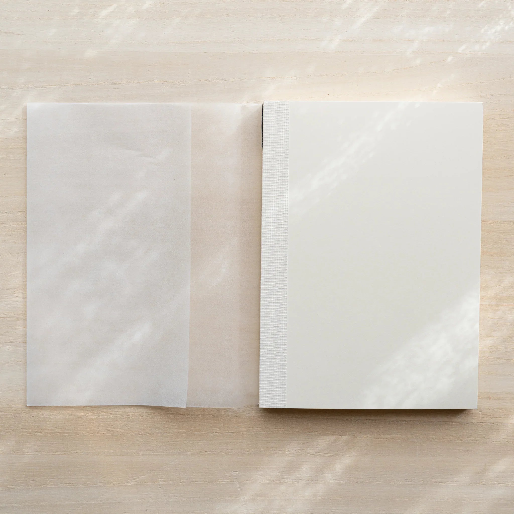 Midori MD Notebook A6 Grid with glassine cover unfolded flat beside closed notebook, thread-stitched spine visible on right