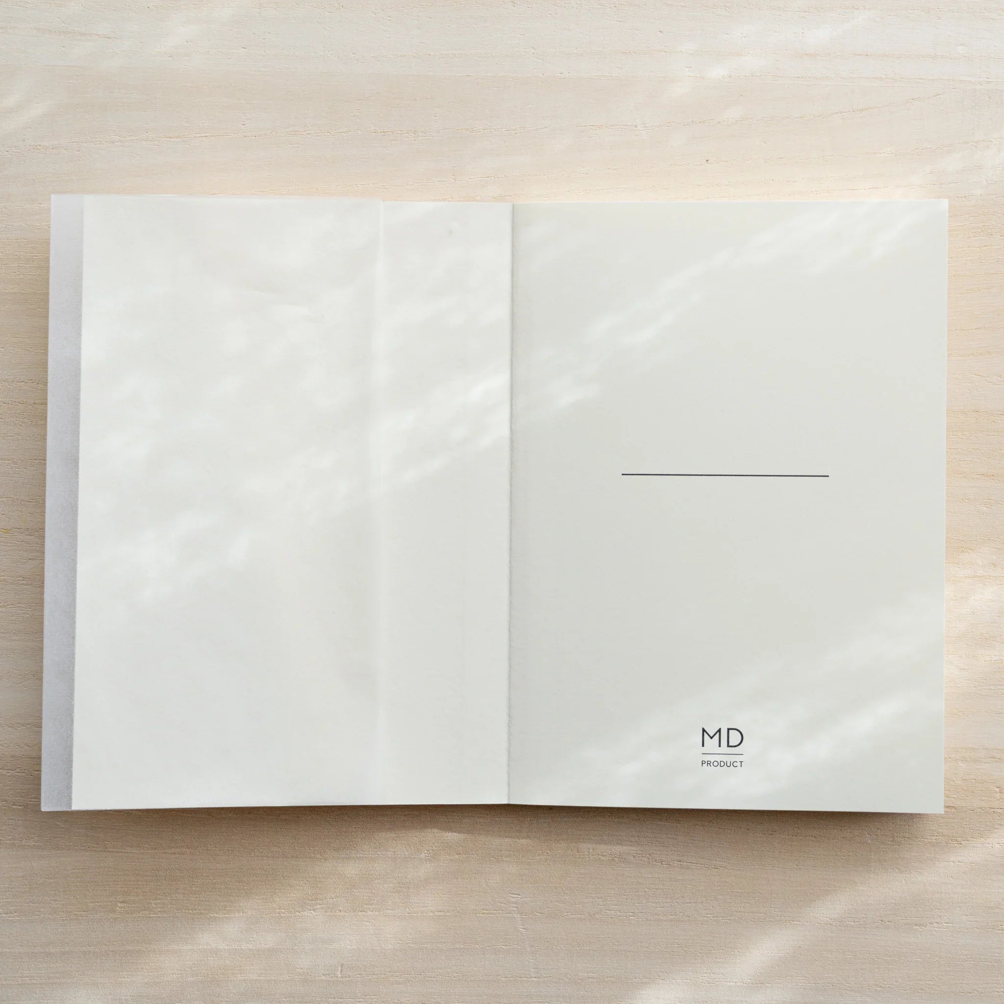 Midori MD Notebook A6 Grid open flat, glassine inner cover on left, white right page with center line and MD Product logo