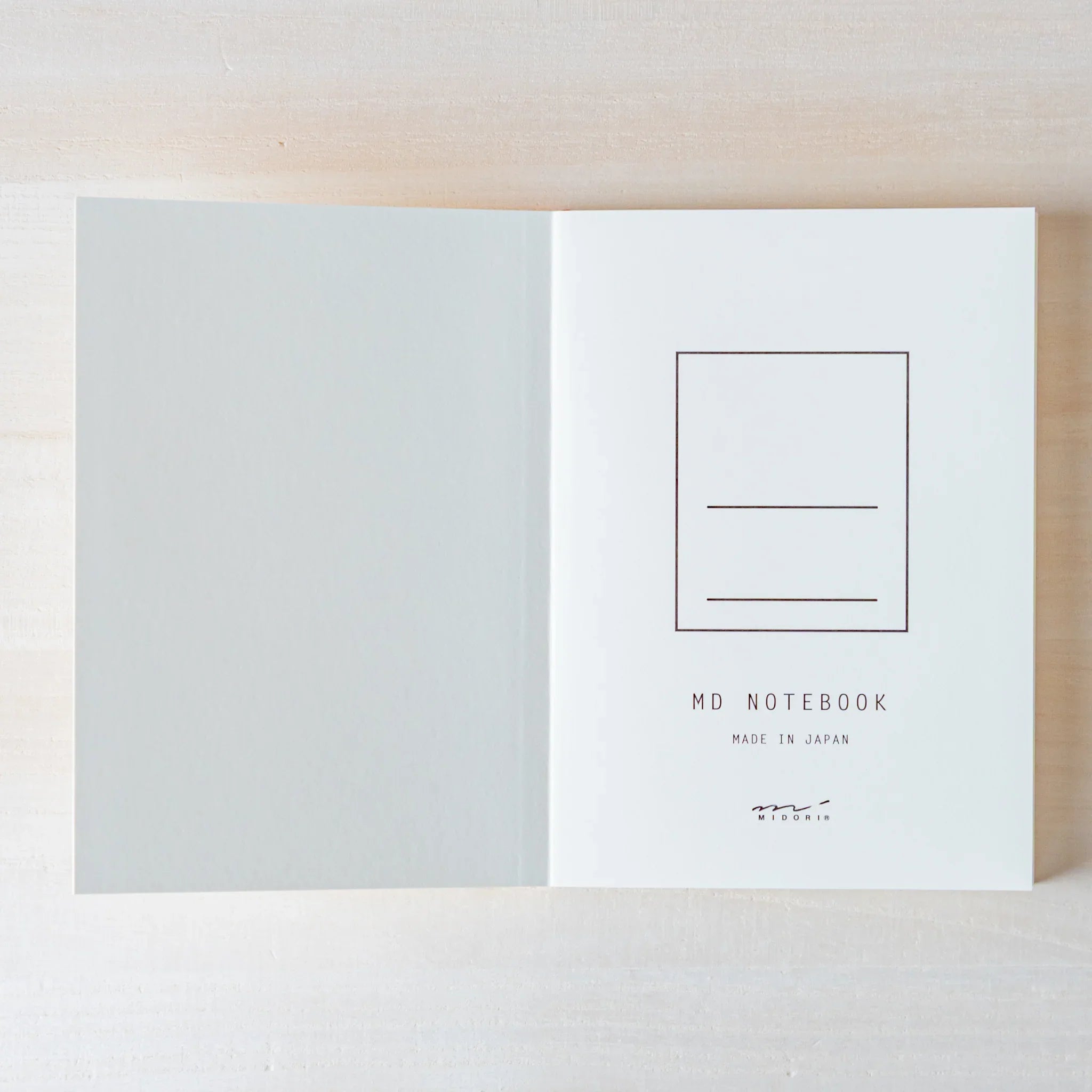 Japanese Notebook Midori MD A6 opened flat, showing a clean blank page spread on a light wooden surface.