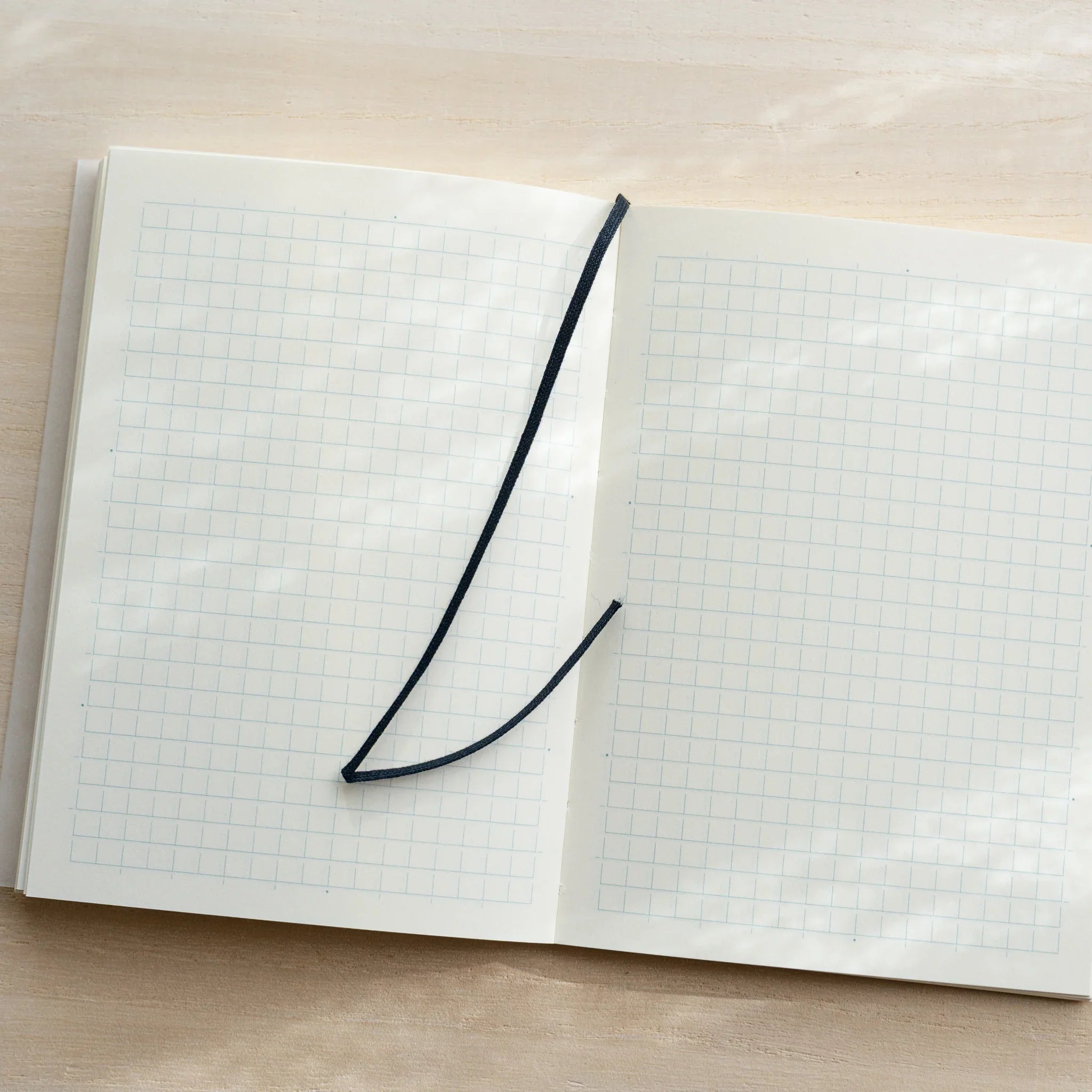 Midori MD Notebook A6 Grid open flat, ivory grid pages with dark blue bookmark ribbon lying diagonally across spread