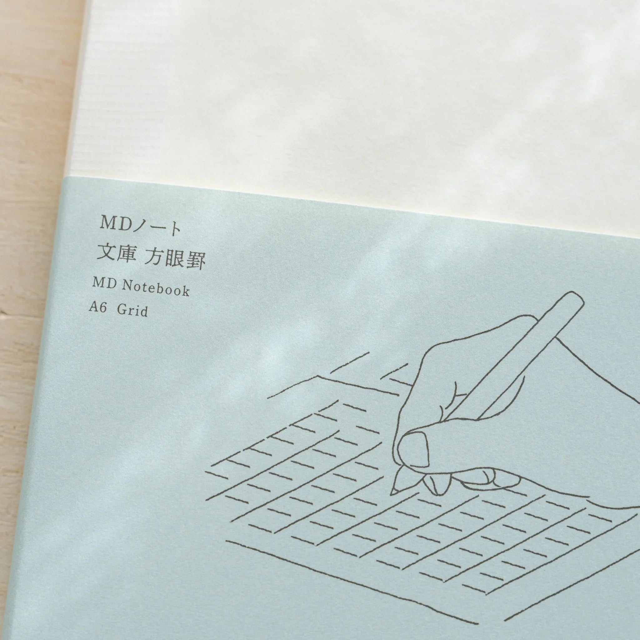 Midori MD Notebook A6 Grid glassine front close-up, teal lower half with hand-writing on grid illustration and product name