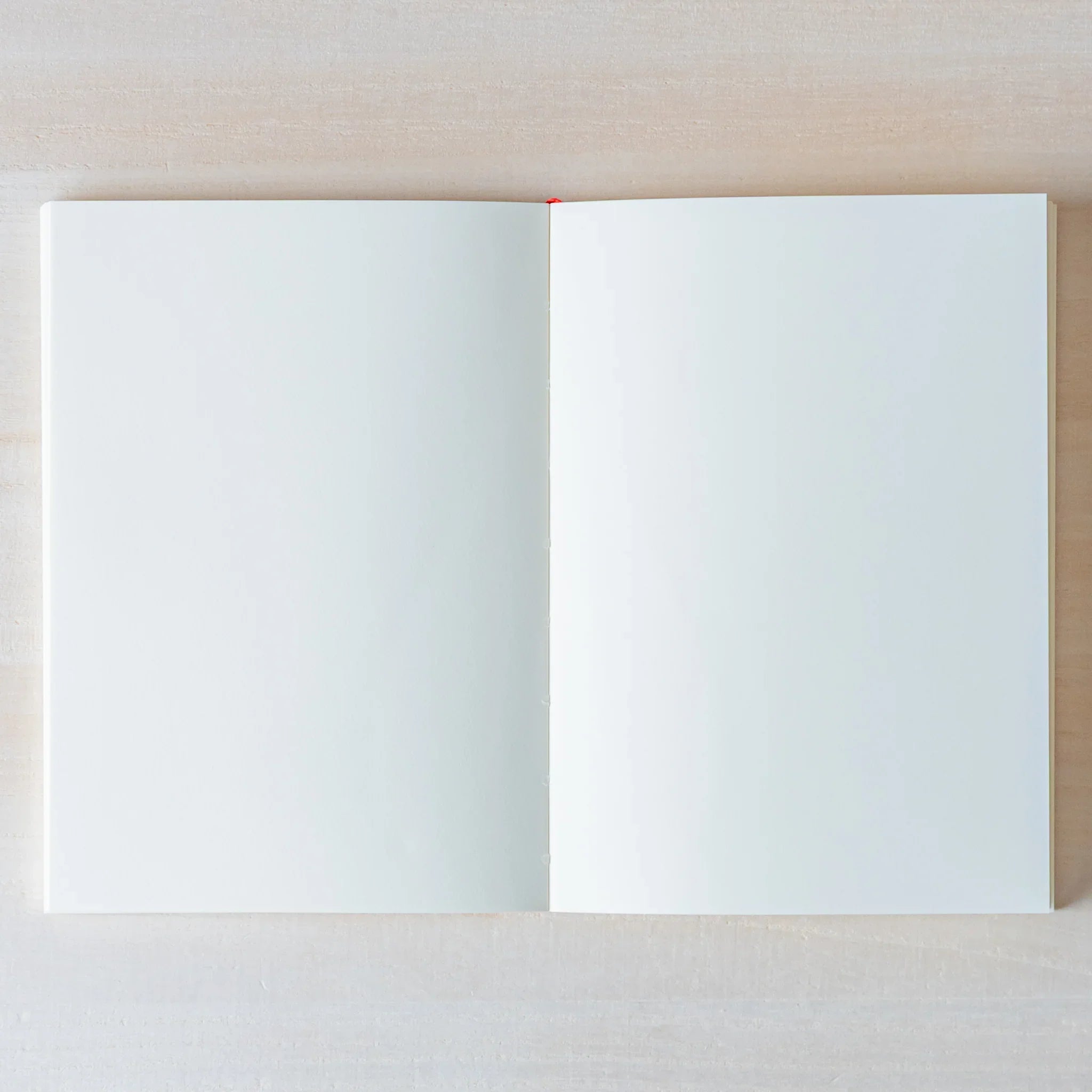 Japanese Notebook Midori MD A6 opened flat on a light wooden surface, showing blank white pages.