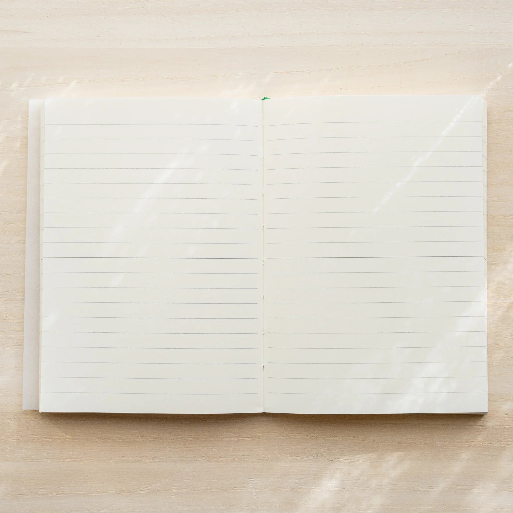 Midori MD Notebook A6 Lined open spread showing ivory lined page spread with horizontal lines, green bookmark ribbon at top