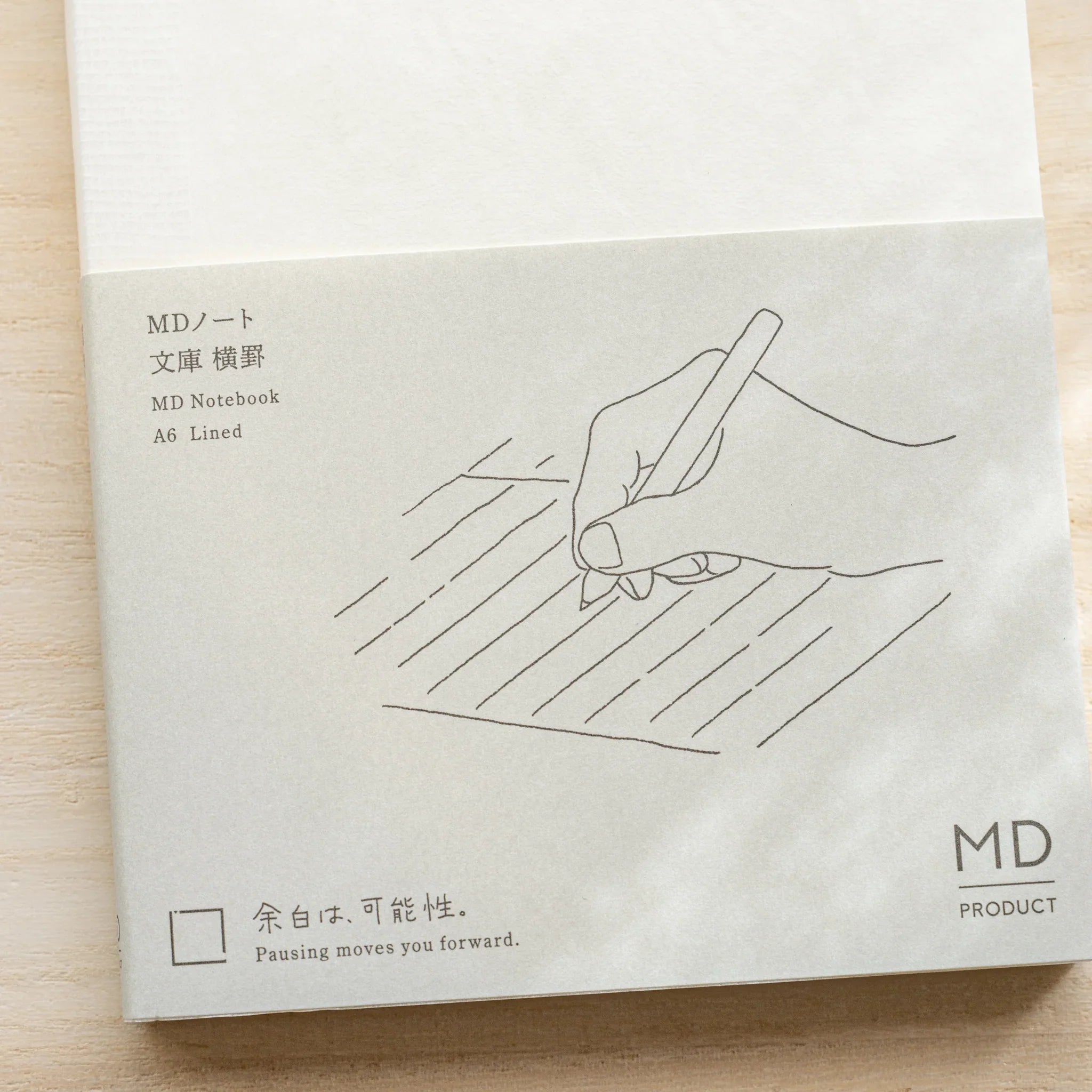 Midori MD Notebook A6 Lined glassine cover laid flat with gray hand-writing illustration, product name and MD Product logo