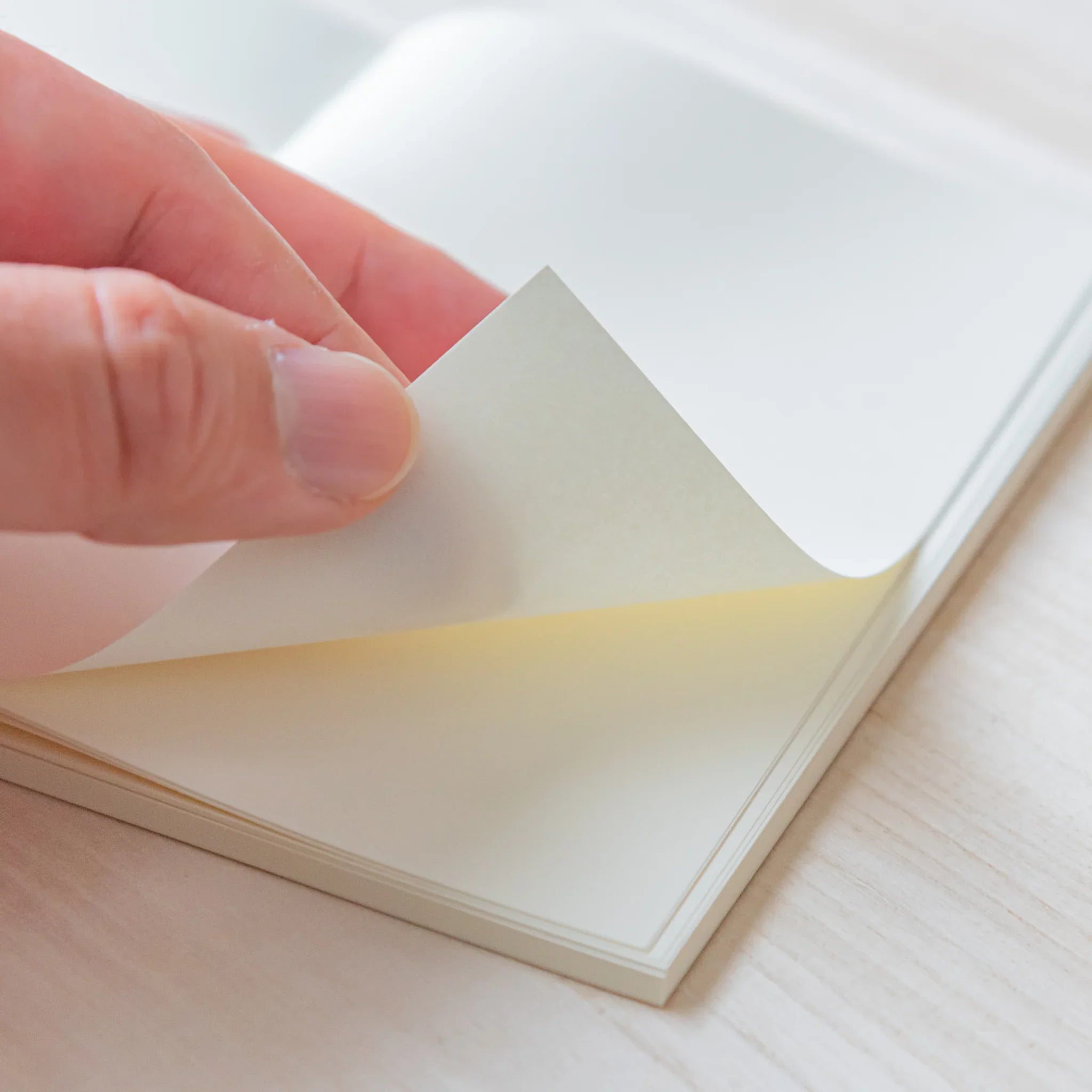 Japanese Notebook Midori MD A6 page being gently turned by hand, showing smooth cream paper.