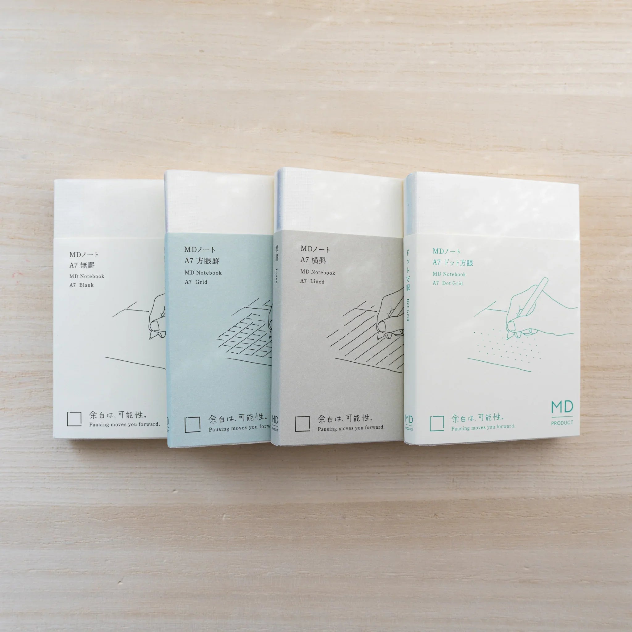 MD Notebook A7 in cream cover with paper belly band showing a hand-with-pen line drawing