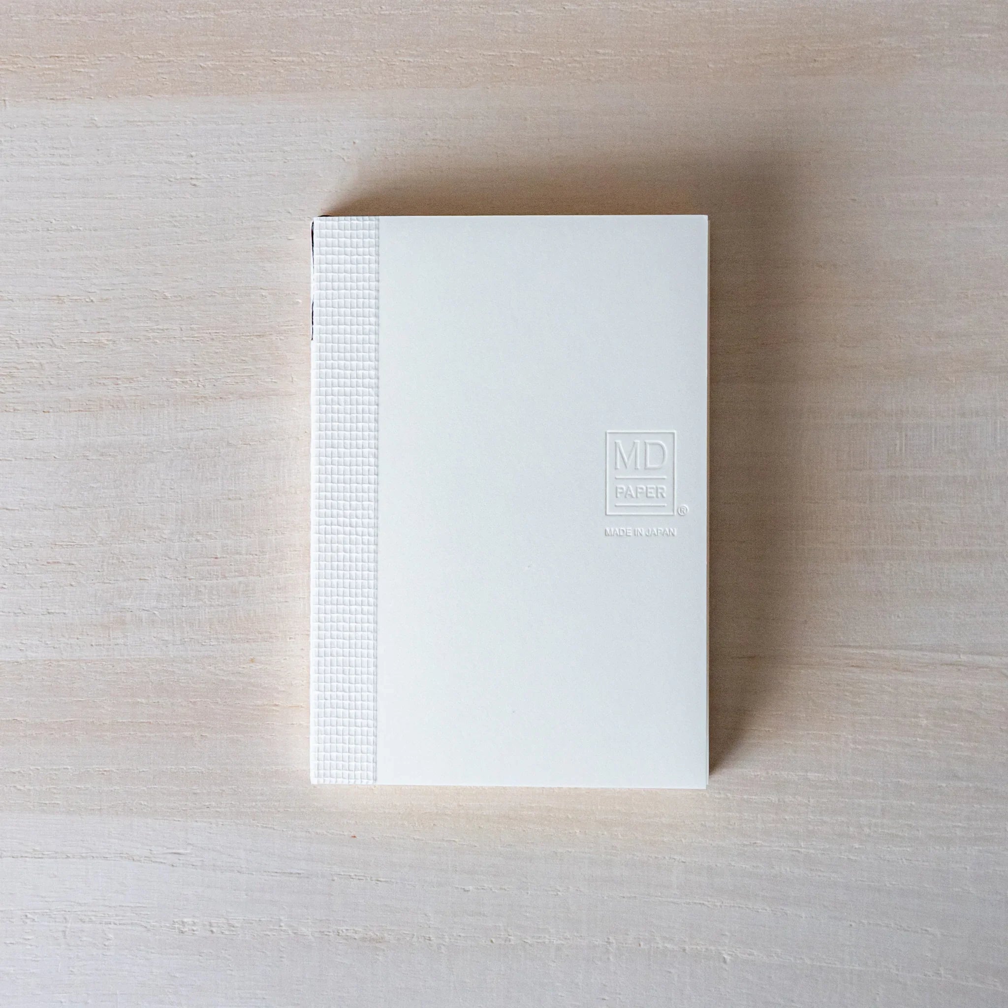 Japanese Notebook front view of a Midori MD A7 notebook with a white cover and embossed MD PAPER logo on a wooden surface.