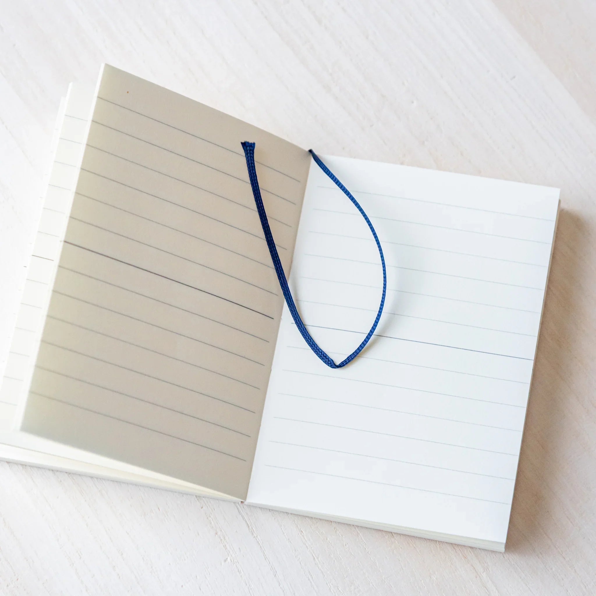Japanese Notebook open lined pages of a Midori MD A7 notebook with a blue ribbon bookmark resting across the spread.