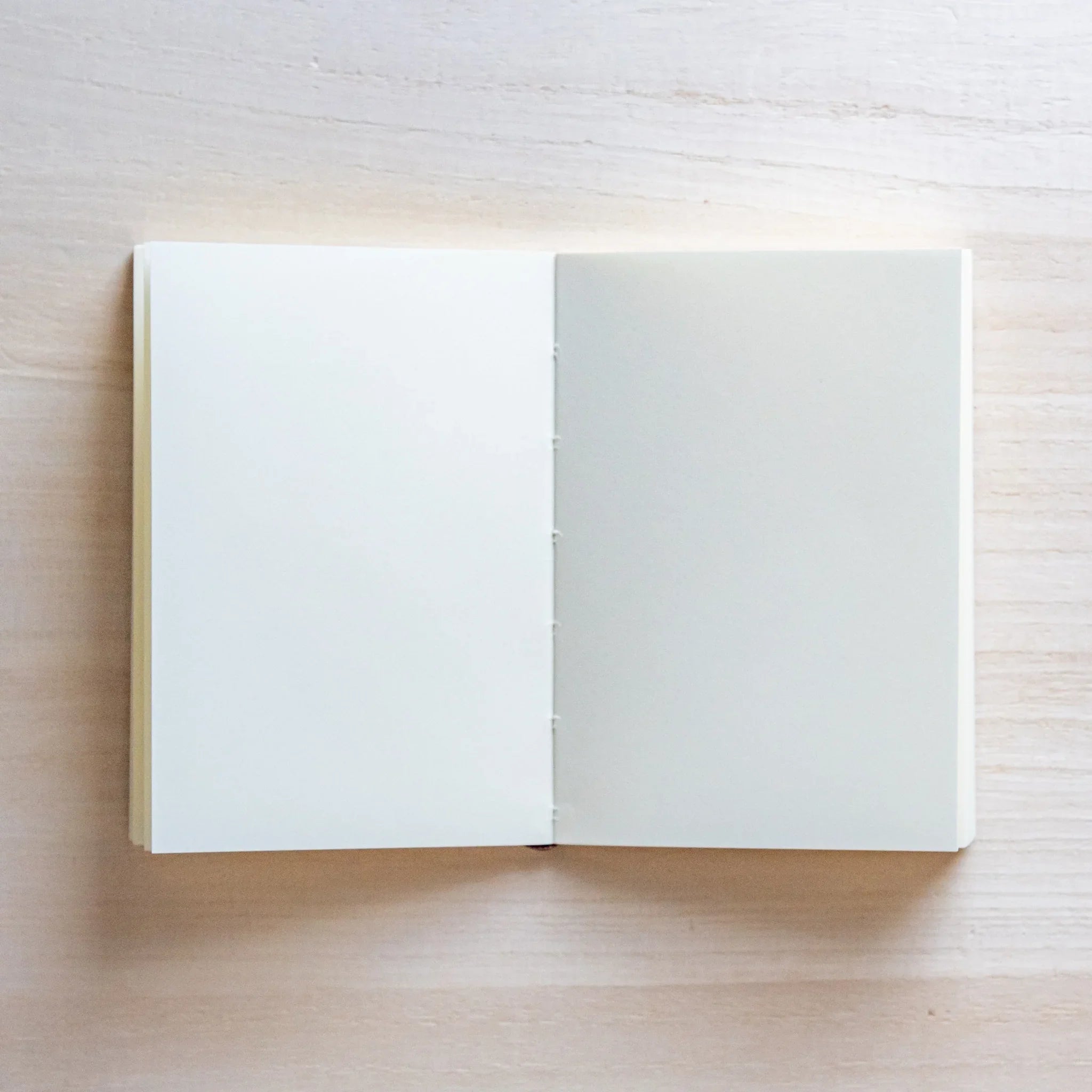 Japanese Notebook open blank pages of a Midori MD A7 notebook laid flat on a light wooden surface.