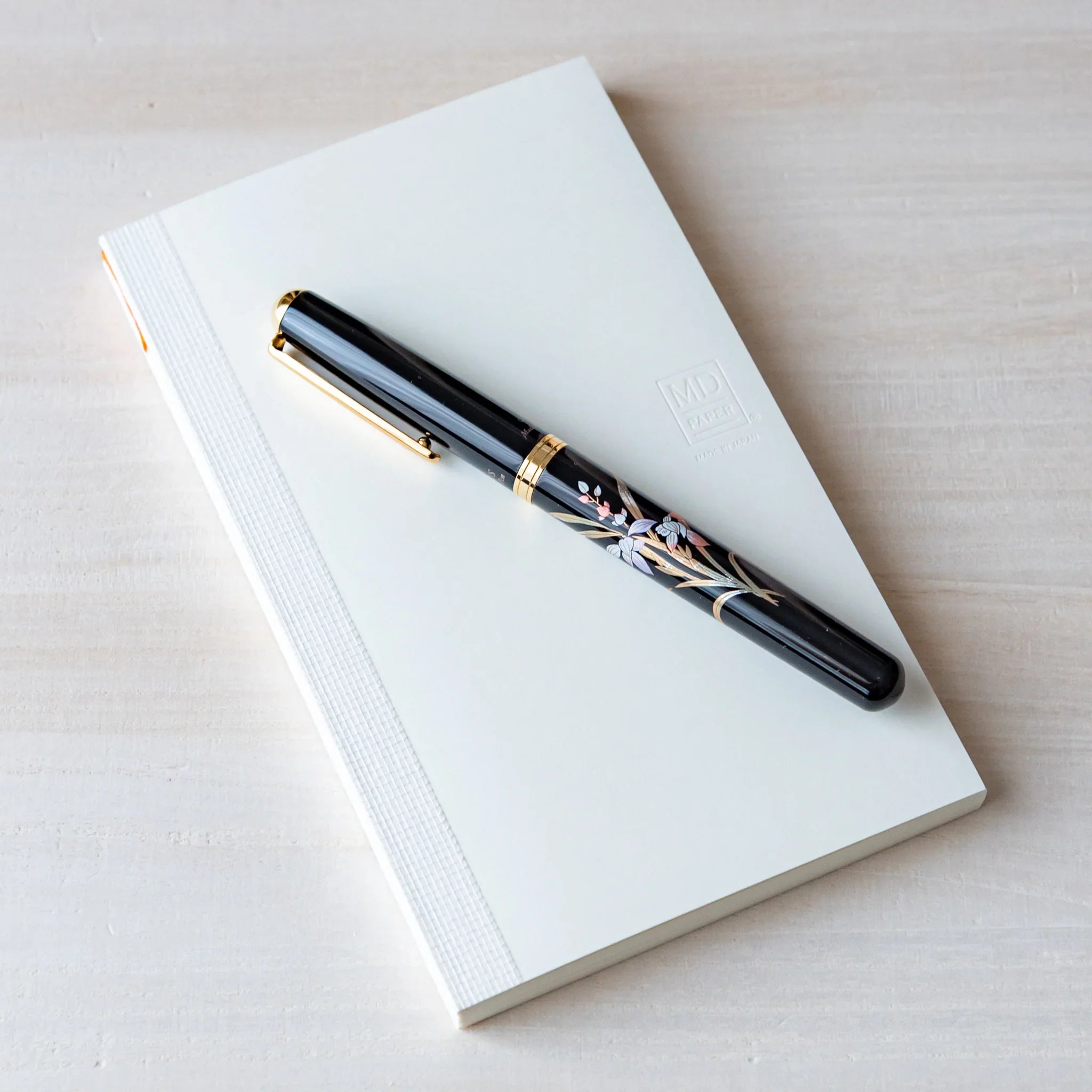 Japanese Notebook top view of a Midori MD B6 notebook with a minimalist white cover, paired with a fountain pen on a wooden surface.