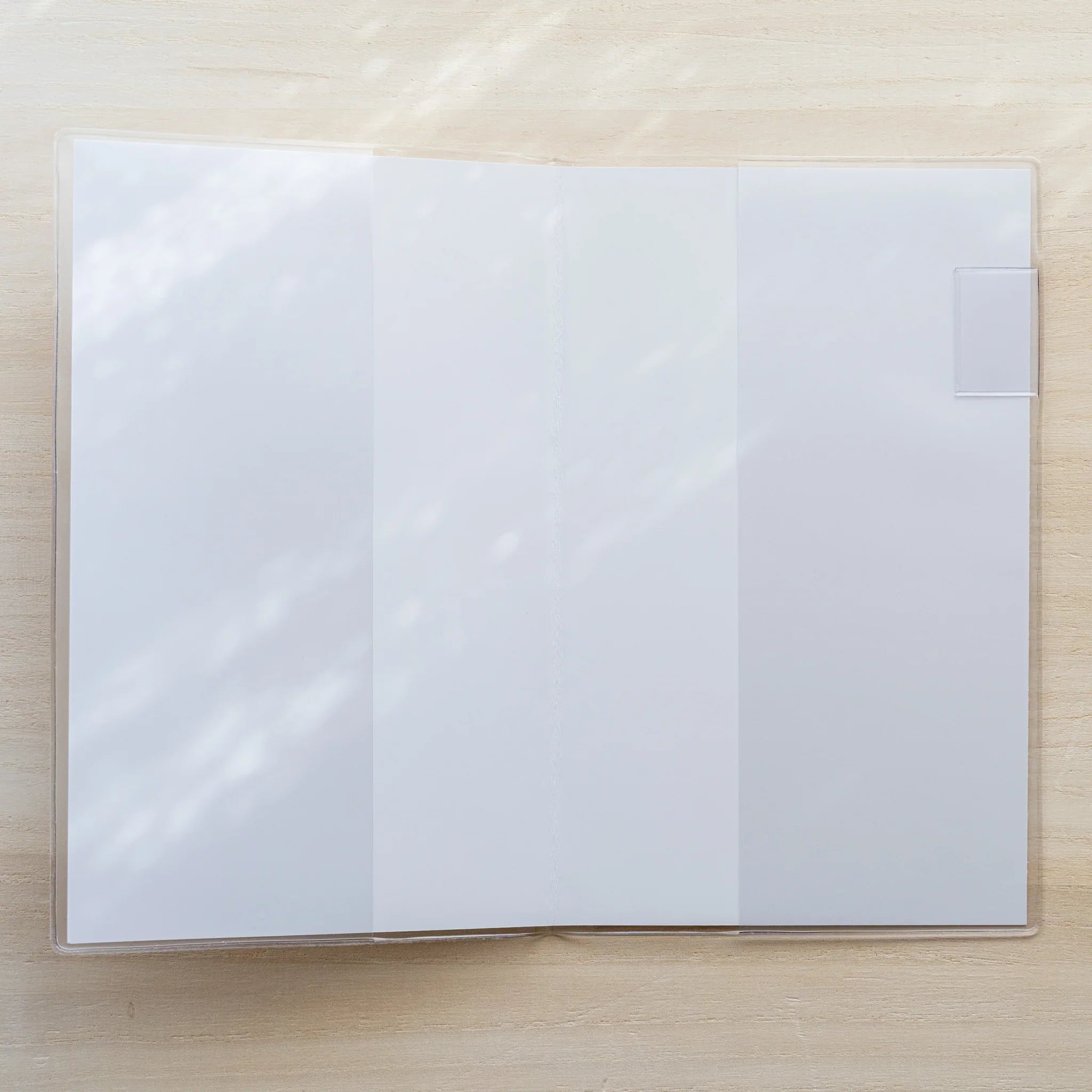 Midori MD Notebook open flat inside clear PVC cover showing blank white spread pages and white bookmark tab on right side