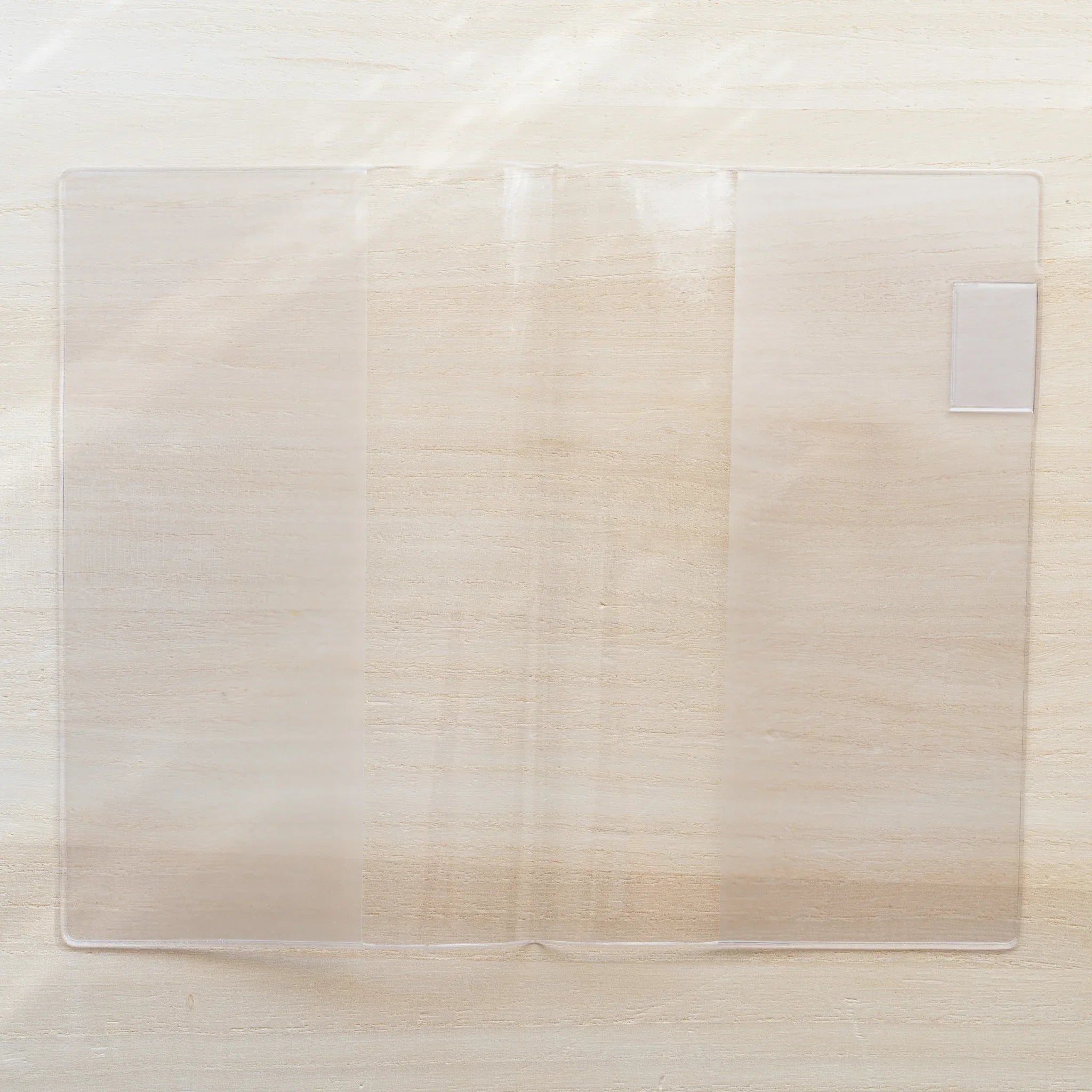 Midori MD Notebook Cover open flat on wooden surface, clear PVC two-panel spread with white bookmark tab visible on right