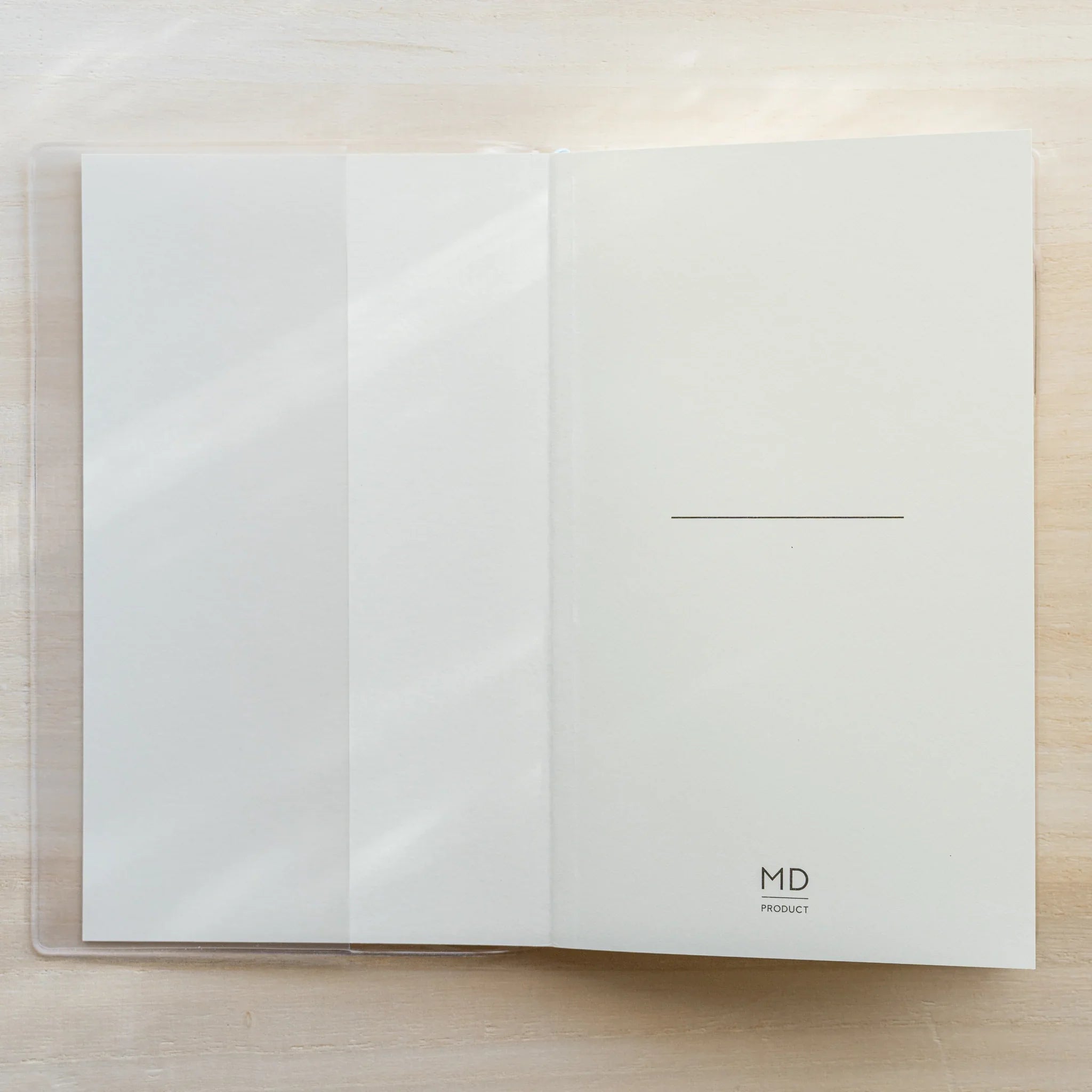 Midori MD Notebook A5 Square in clear PVC cover on wooden surface, white cover with center line and MD PRODUCT logo visible