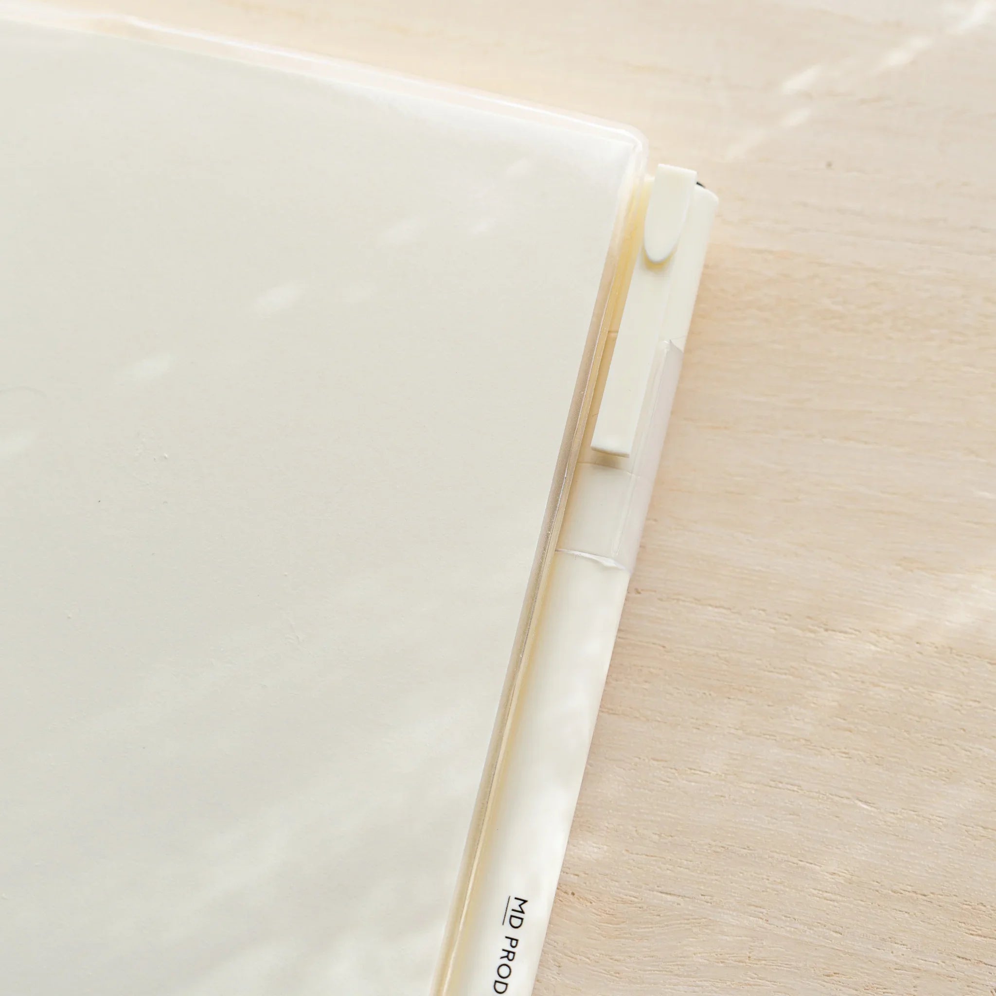 Close-up of MD Notebook Cover A5 right side with white MD PRODUCT pen tucked in pen holder slot on clear PVC edge