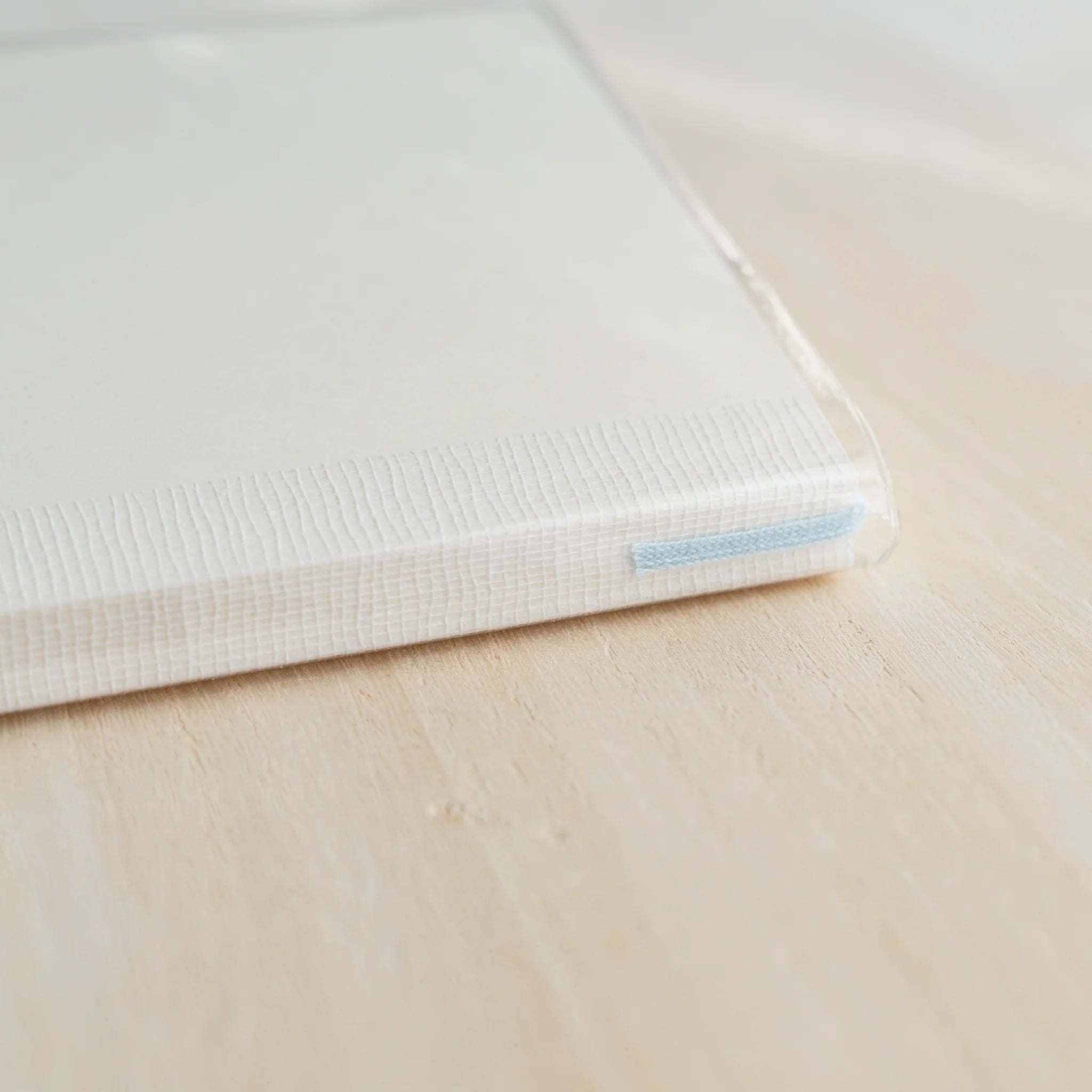 Close-up of MD Notebook Cover A5 top-left corner showing ribbed cloth spine and blue ribbon bookmark under clear PVC edge