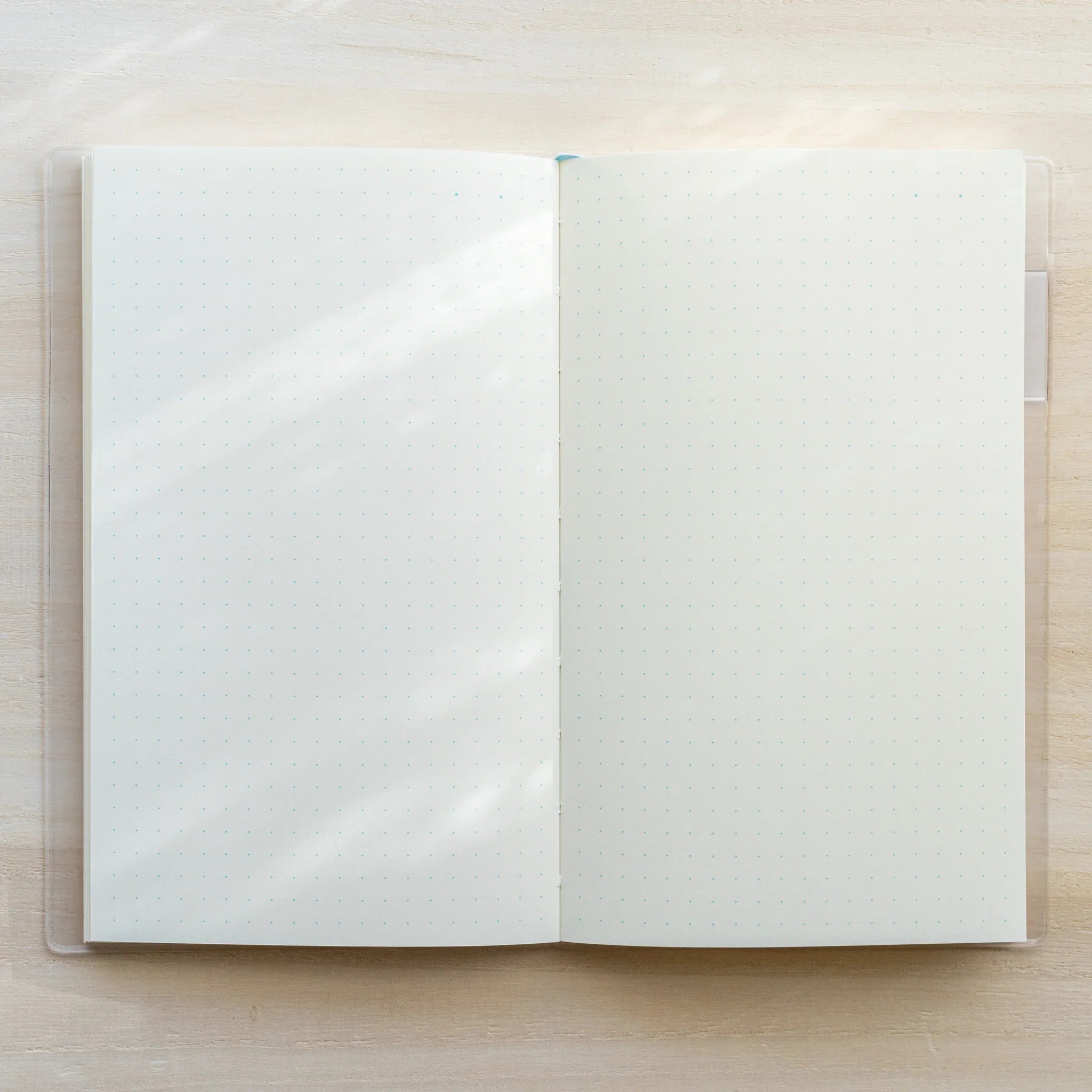 MD Notebook A5 open flat in clear PVC cover showing blank white spread, center spine, and white bookmark tab on right side