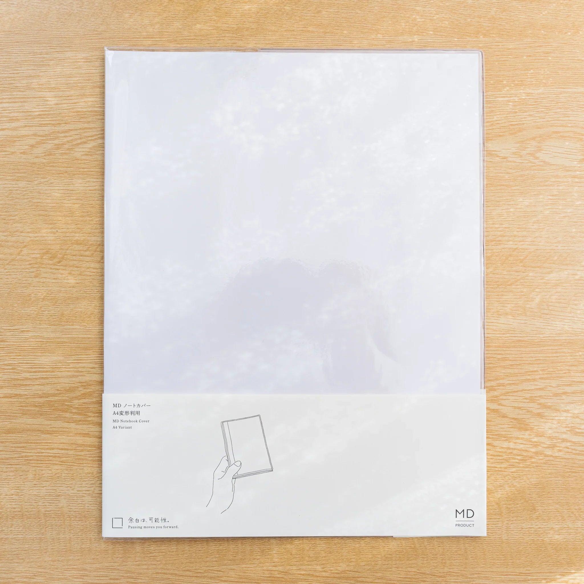 Midori MD Notebook Cover A4 Variant, clear cover fitted on a white MD notebook with paper belly band, on wood desk