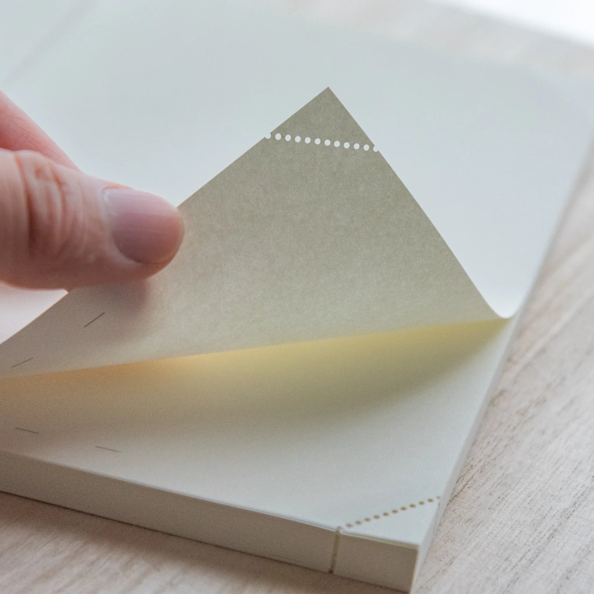 Hand holding a single beige page of Midori Japanese journal with perforated corner against light background.