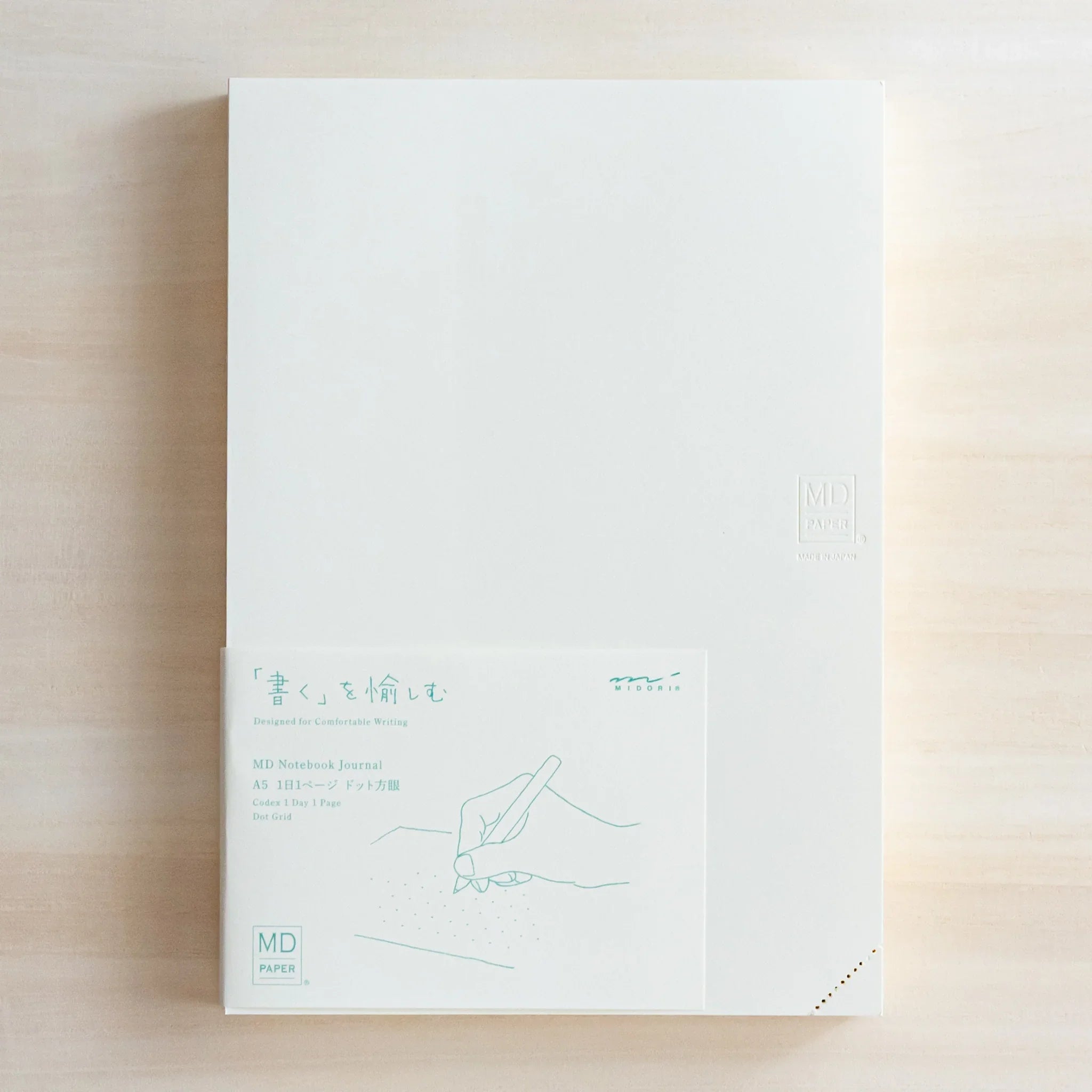 Top view of Midori Japanese journal with plain white cover and illustrated information card showing hand drawing.