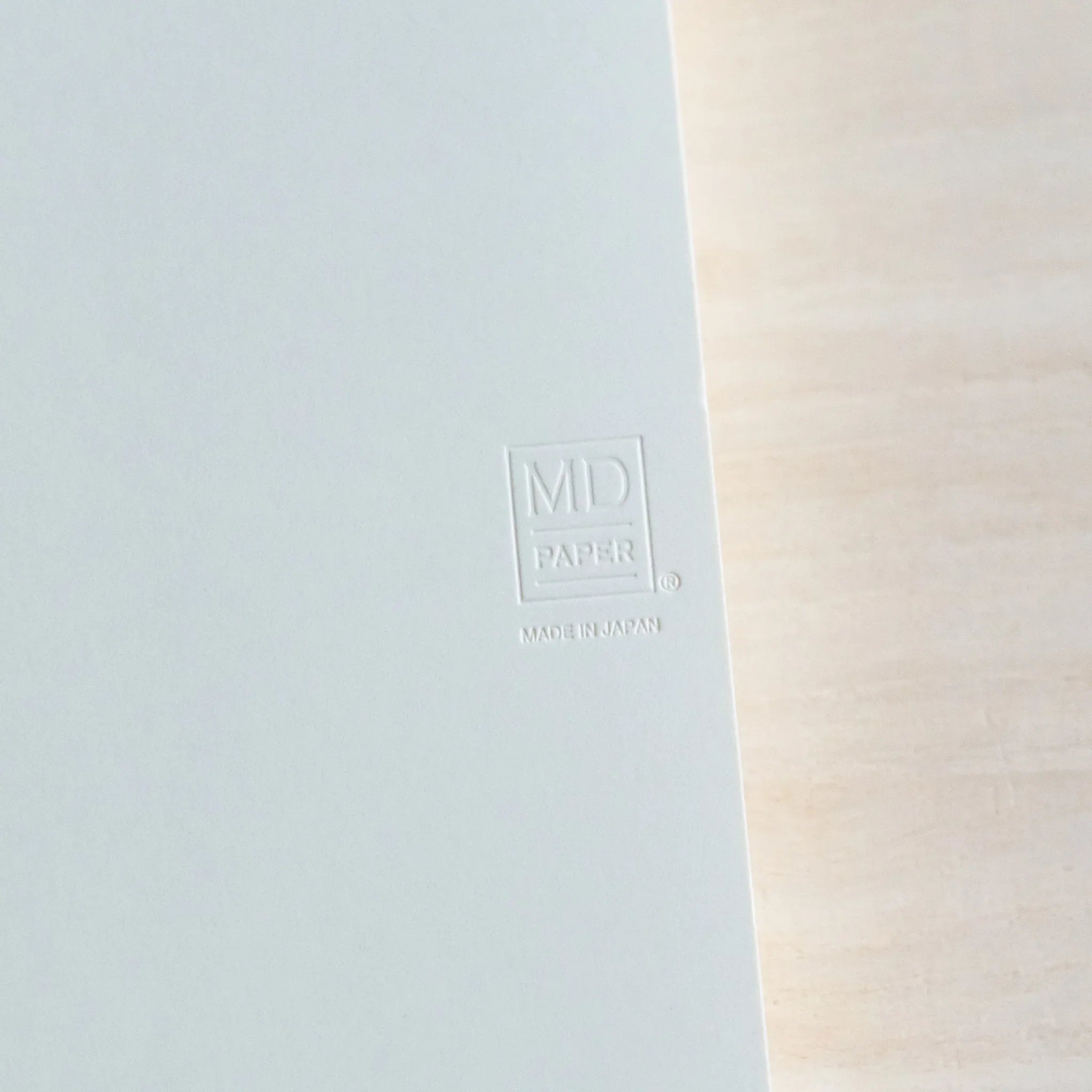 Close-up of Midori Japanese journal white cover with embossed MD Paper logo on light wood.