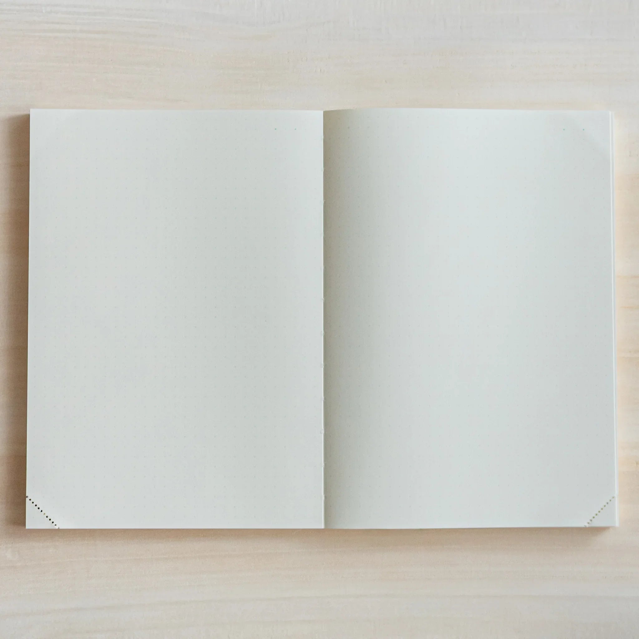 Top view of open Midori Japanese journal with two blank pages on light wood surface.
